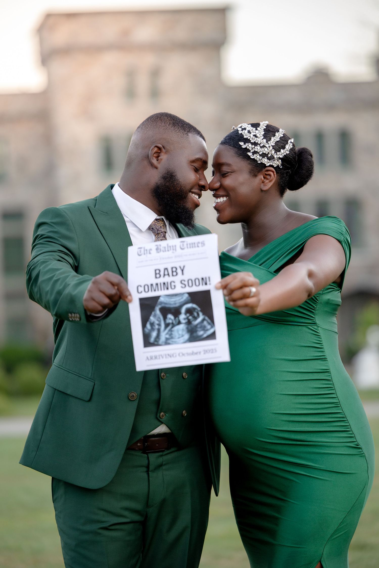 Couple in matching green outfits holding Baby Coming Soon newspaper sign for pregnancy announcement.