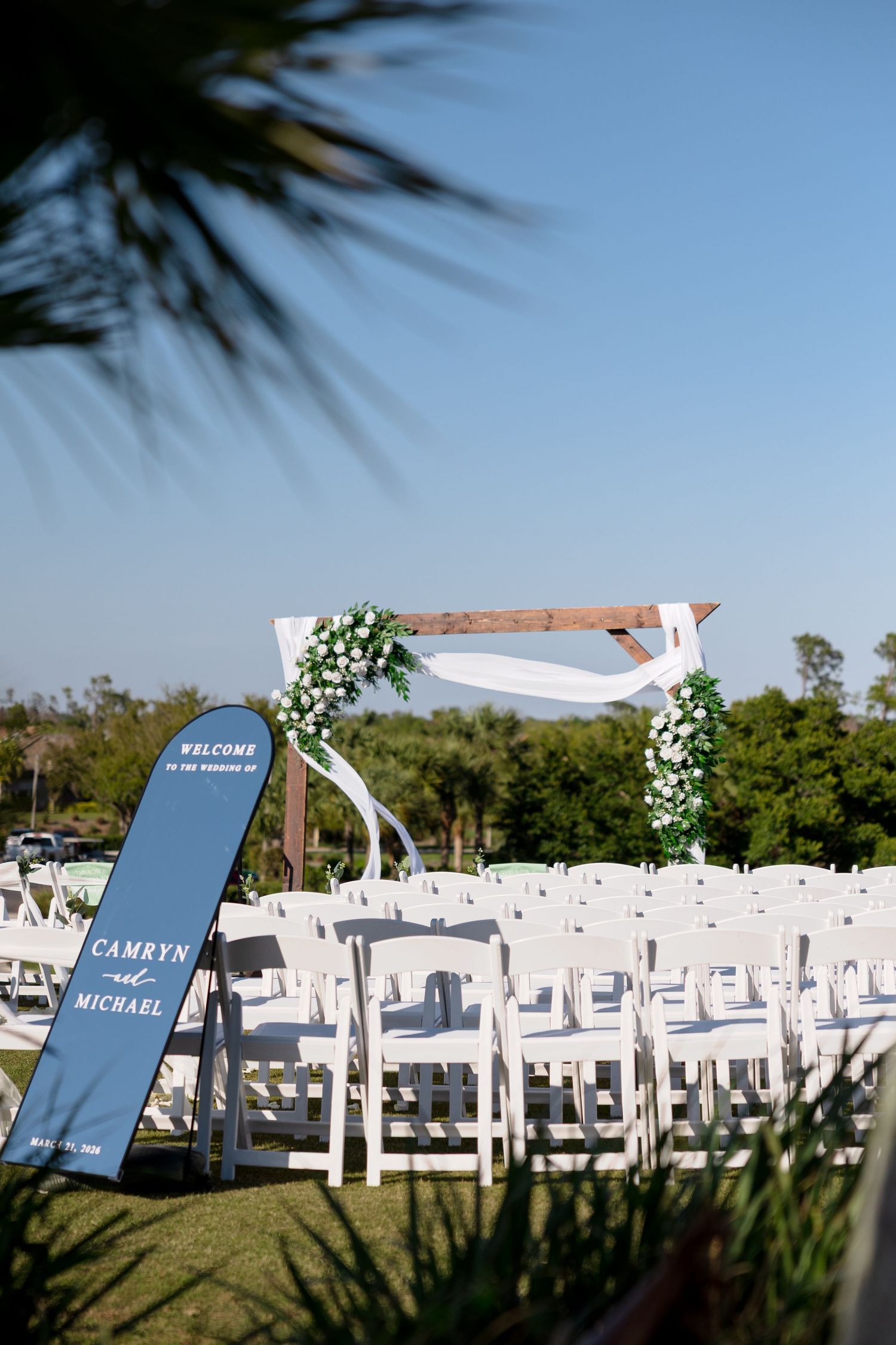 Outdoor wedding ceremony setup with floral arch and welcome mirror at Lido Beach Resort in Sarasota, Florida, captured by Grand Photo