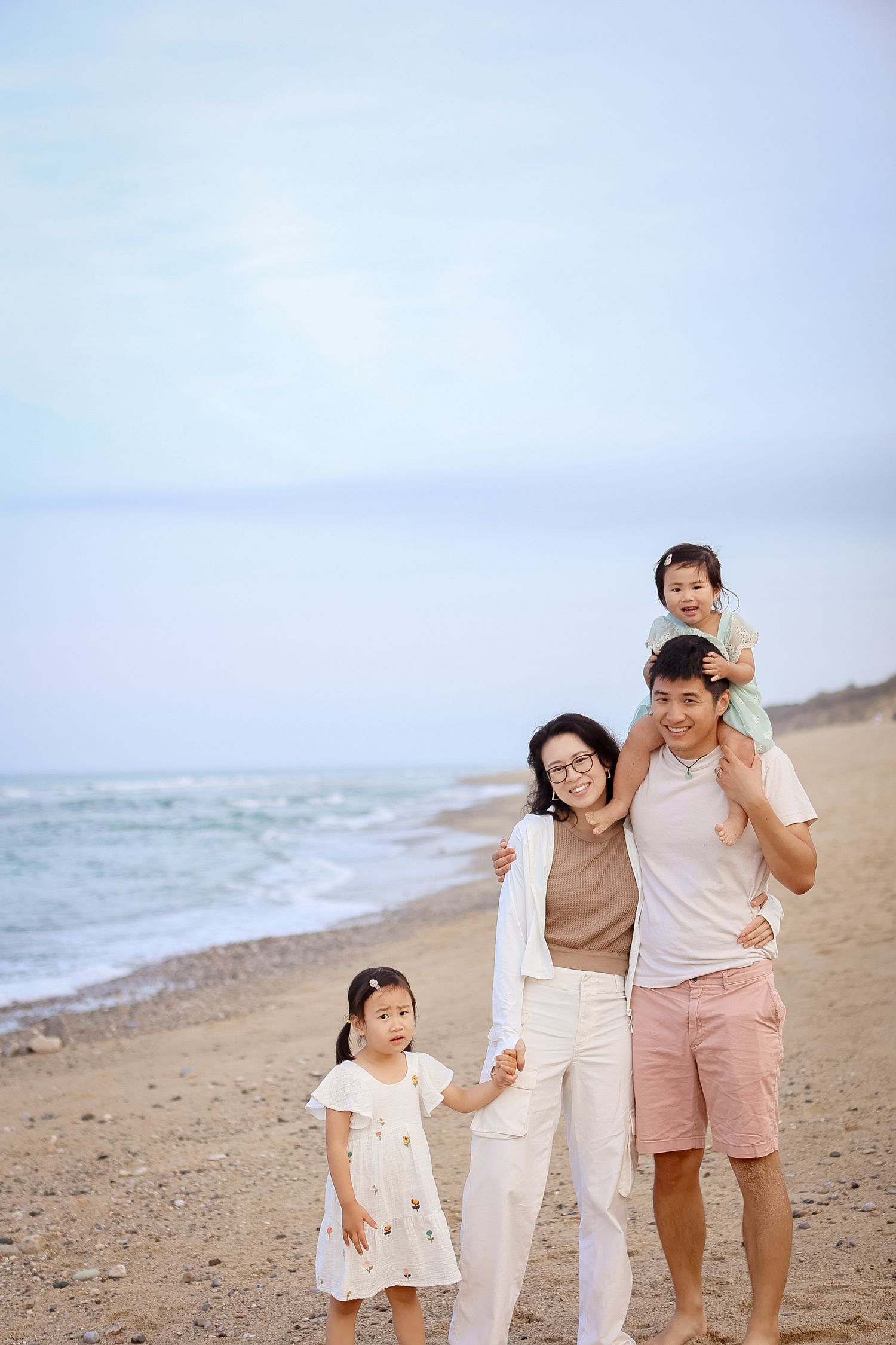 Asian family of four walking on the beach, with young daughter on father's shoulders.