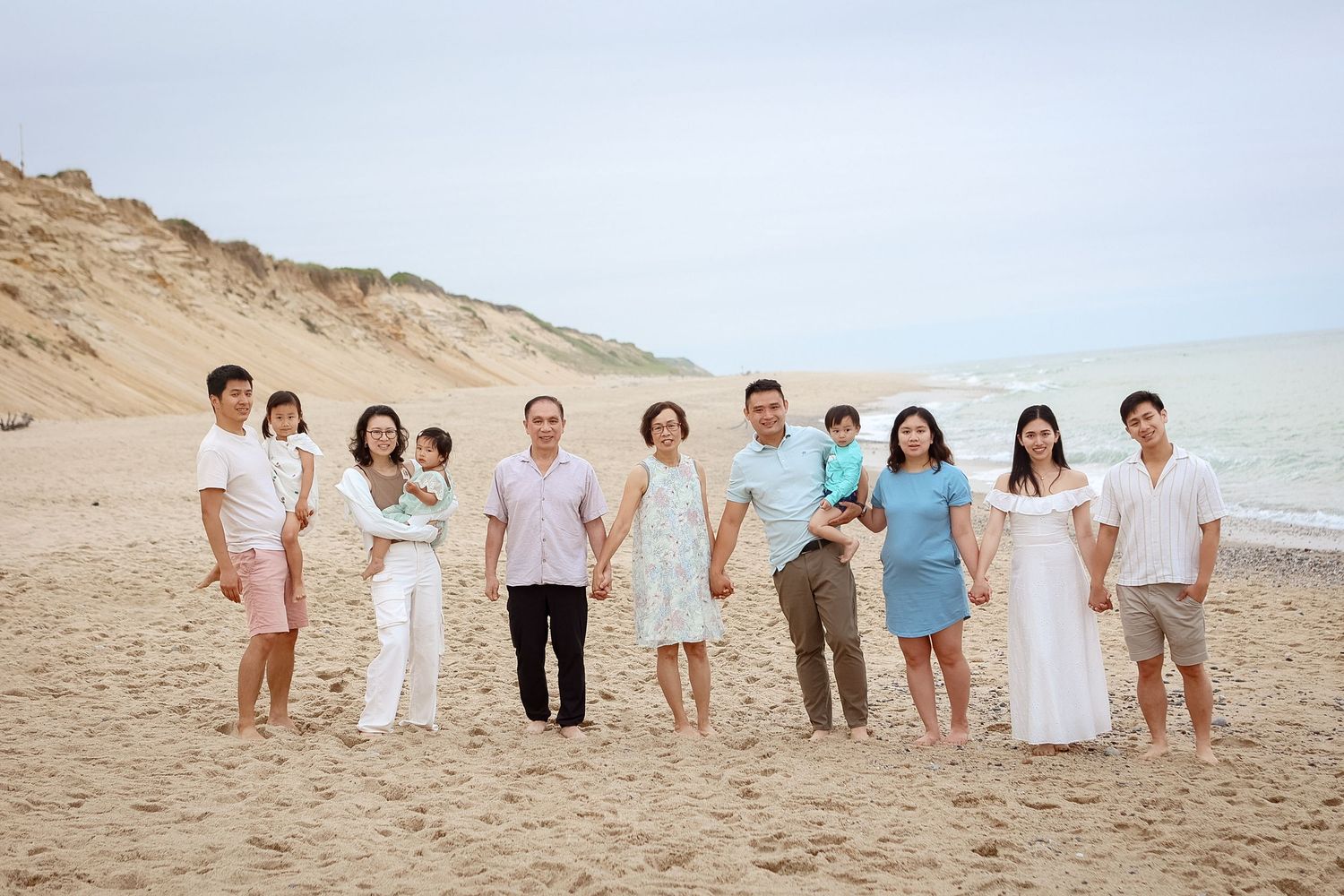 Large Asian family posing together on a sandy beach with coastal cliffs in the background.
