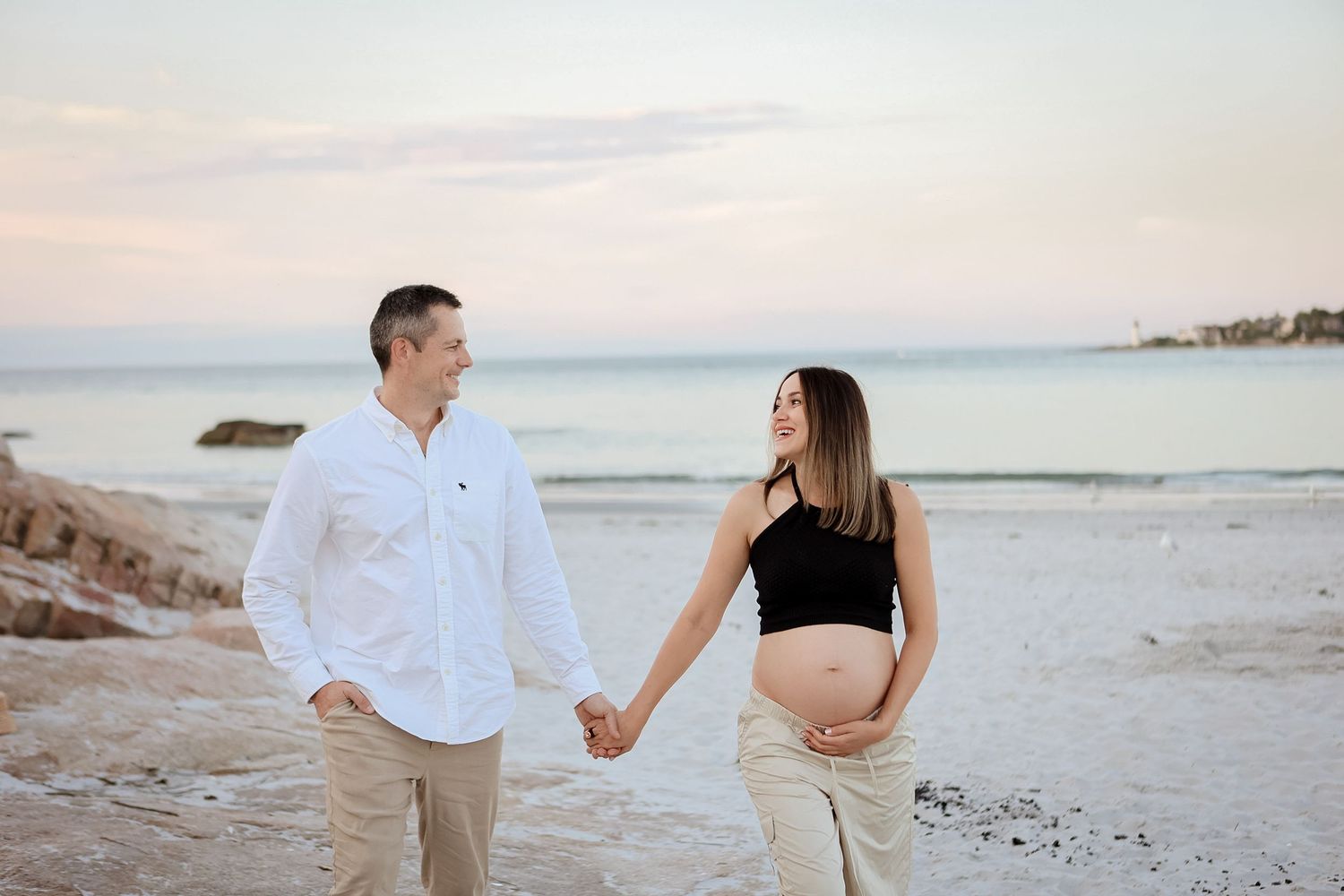 Expecting couple holding hands on beach at sunset during romantic maternity photoshoot.