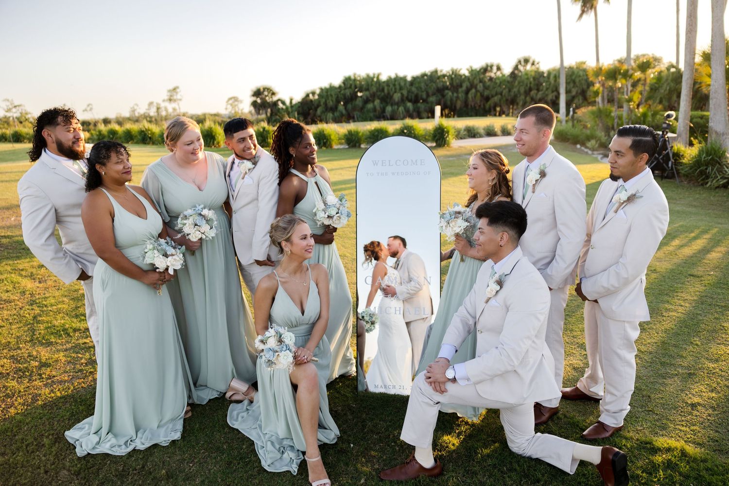 Wedding party gathered around bride and groom by a mirror at Heron Creek Golf & Country Club in North Port, Florida, captured by Grand Photo