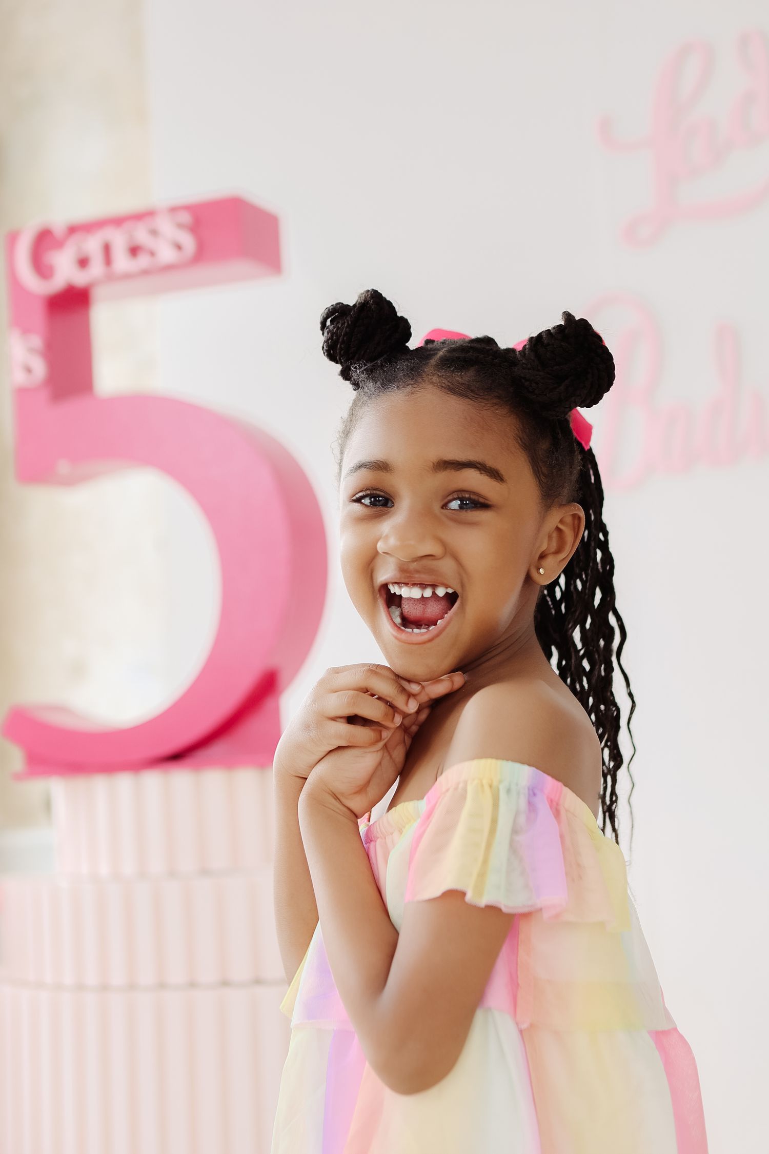 Happy girl in rainbow off-shoulder dress posing at her Genesis 5th birthday party backdrop.