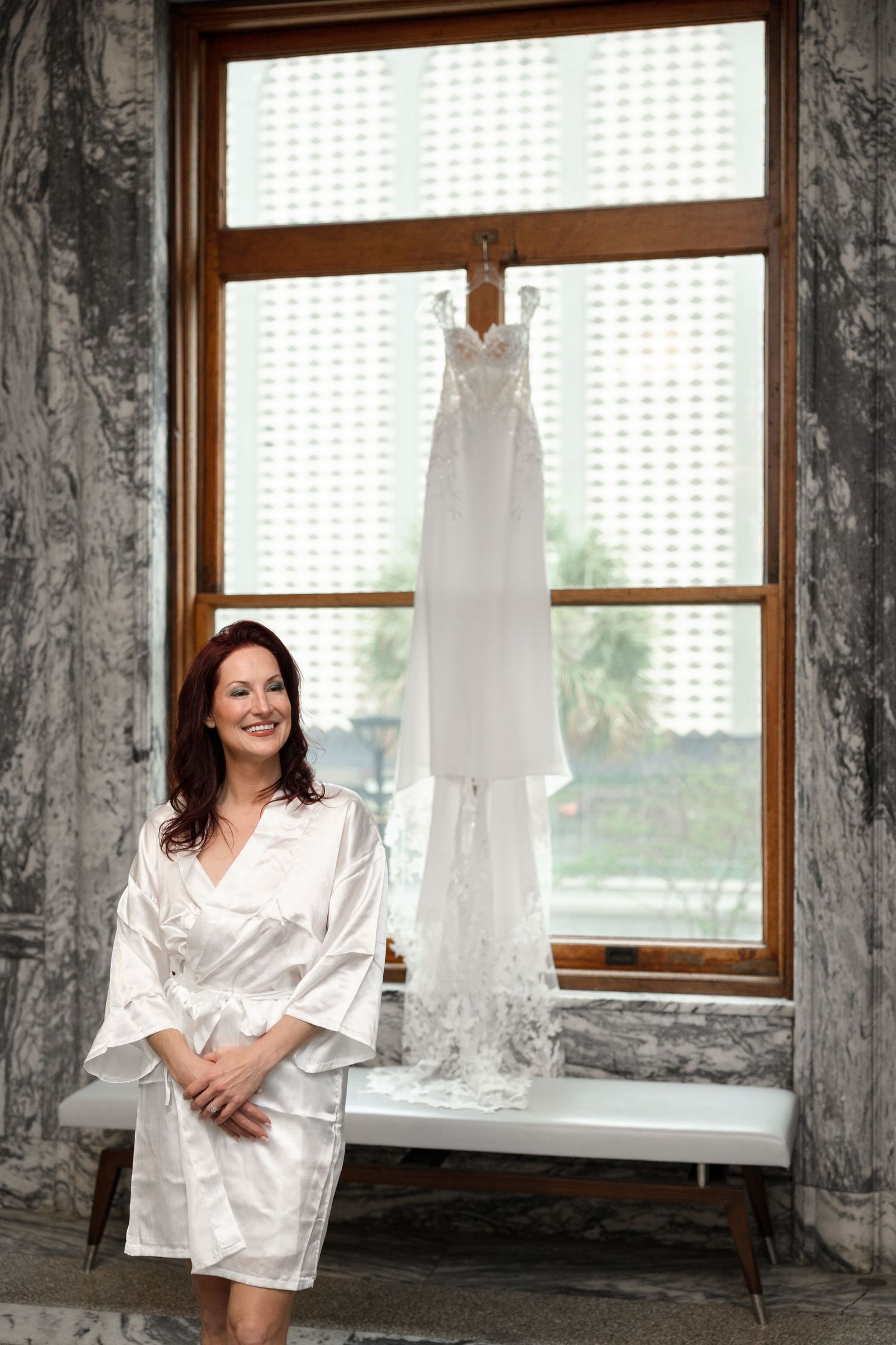 Bride looking at her wedding dress hanging on window at Le Méridien Tampa, Florida, captured by Grand Photo by Karyna Oliinyk