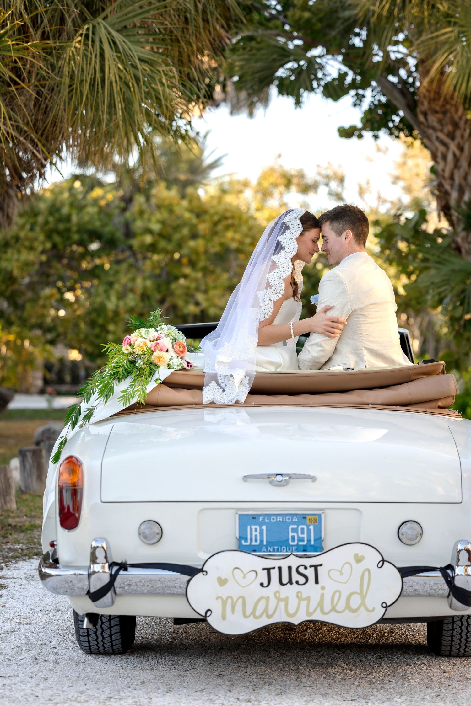 Newlyweds in a vintage white convertible with ‘Just Married’ sign at The Ringling in Sarasota, Florida, captured by Grand Photo