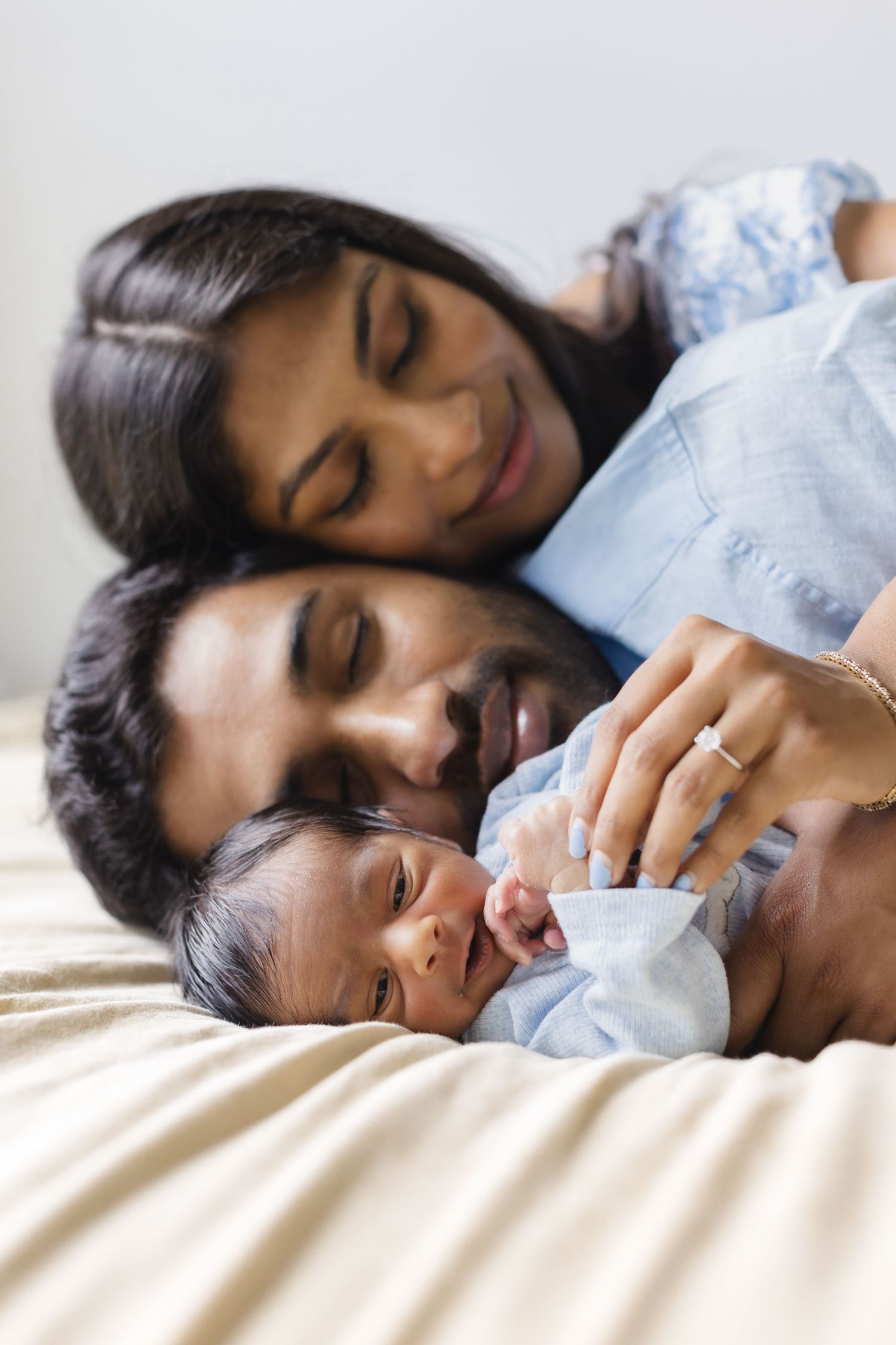 South Asian parents cuddling with their newborn baby on a bed.