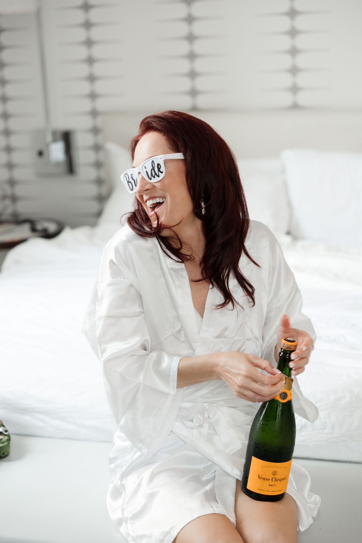 Laughing bride opens champagne during wedding morning preparations at Le Méridien Tampa, Florida, captured by Grand Photo by Karyna Oliinyk