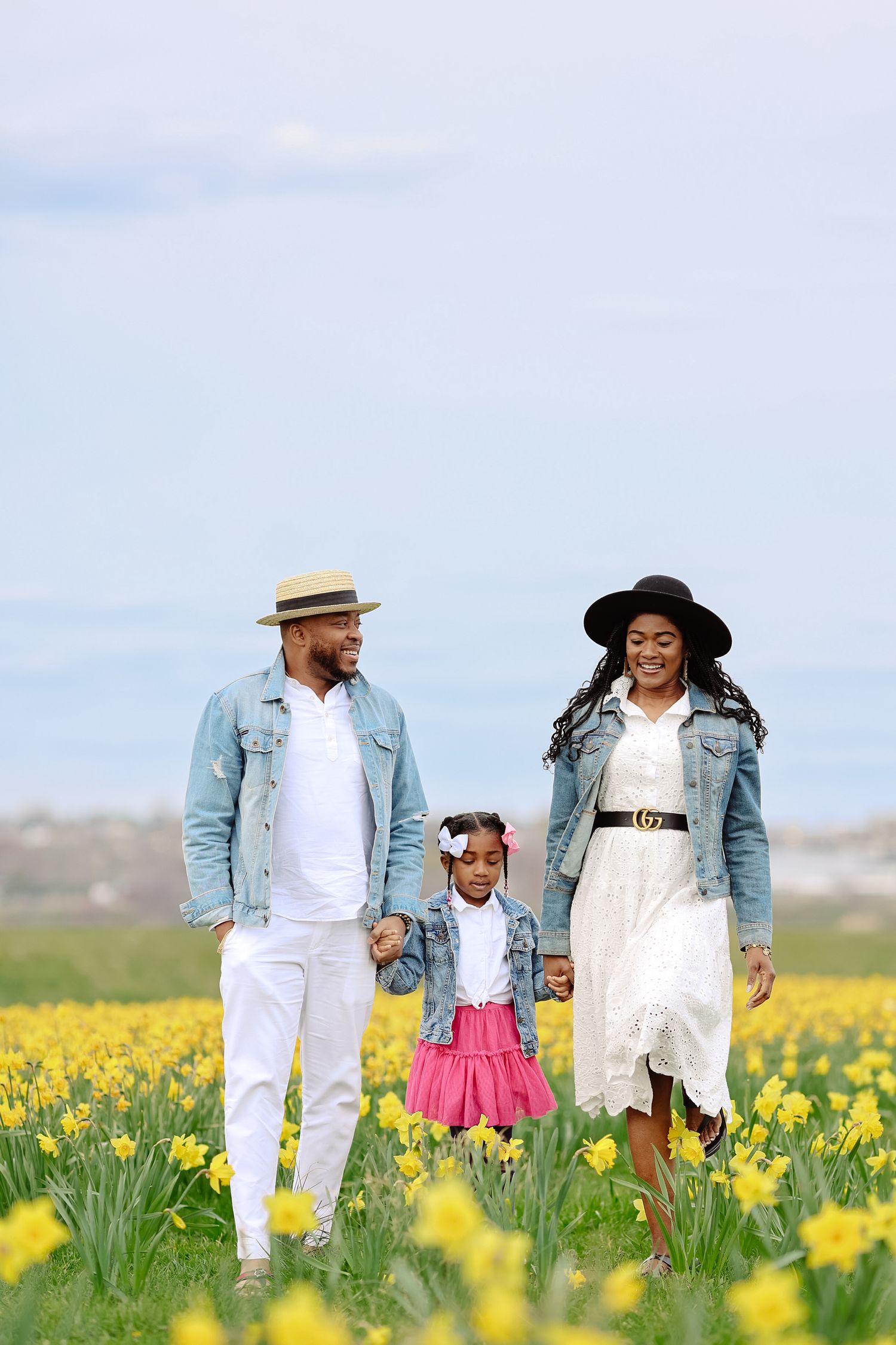 Black family of three walking hand-in-hand through vibrant yellow daffodil field on sunny day.