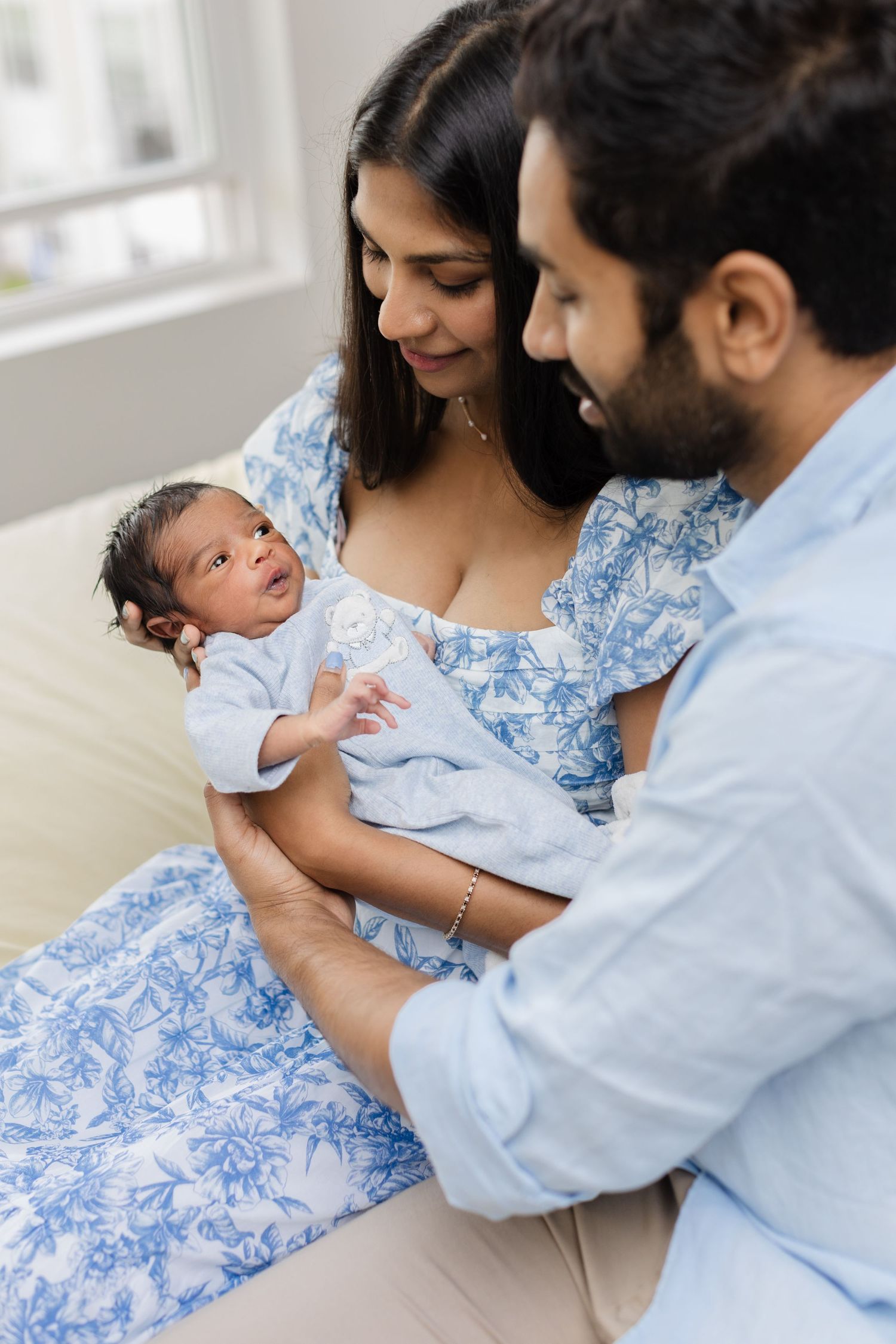 Indian couple admiring their newborn baby on a bed at home.
