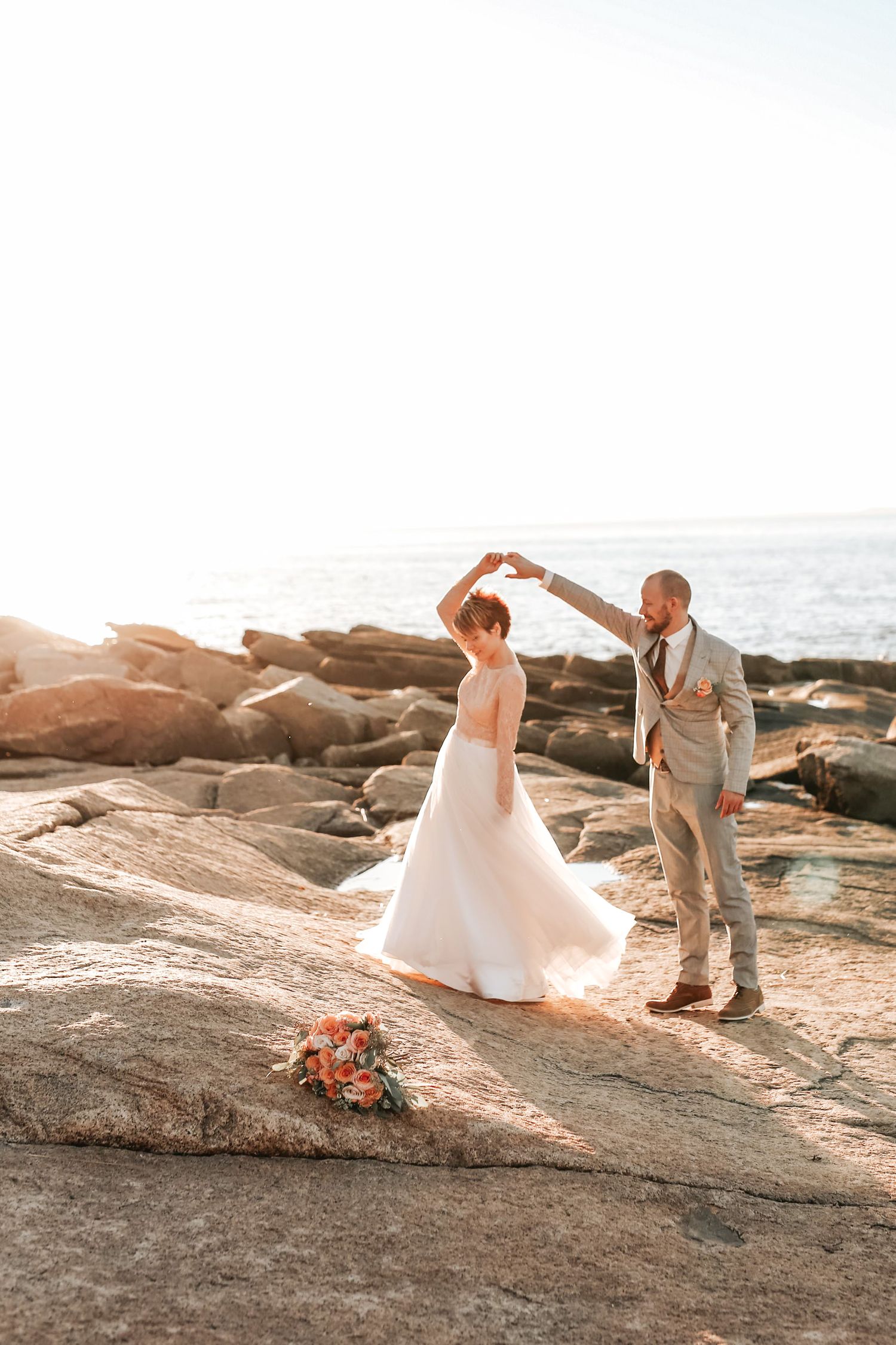Groom twirls bride on rocky coastal cliffs at The Chanler at Cliff Walk in Newport, Rhode Island, captured by Grand Photo by Karyna Oliinyk