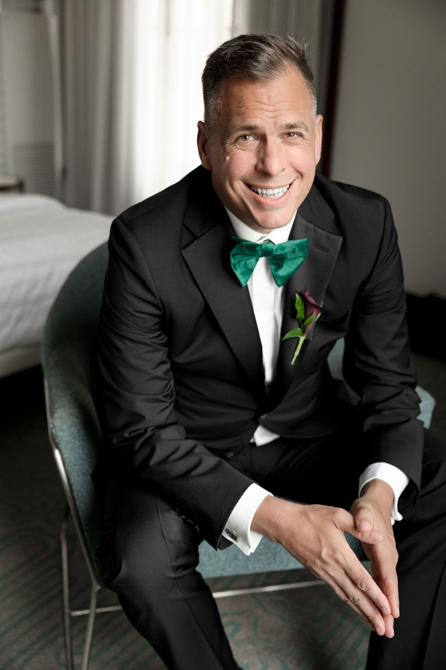 Smiling groom in black tuxedo with green bow tie at Le Méridien Tampa, Florida, captured by Grand Photo by Karyna Oliinyk