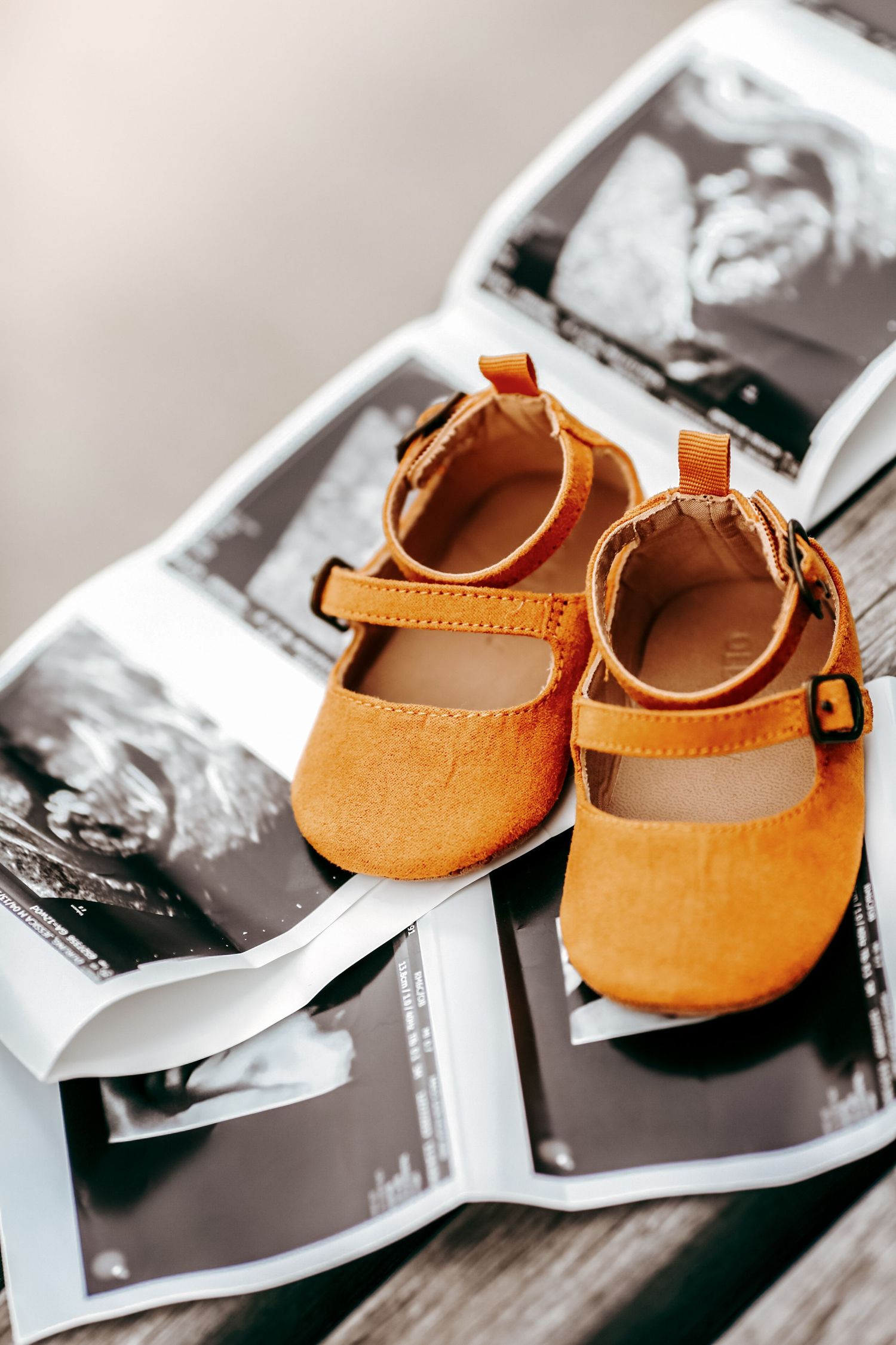 Tiny orange baby shoes placed on black and white ultrasound photos on wooden surface.