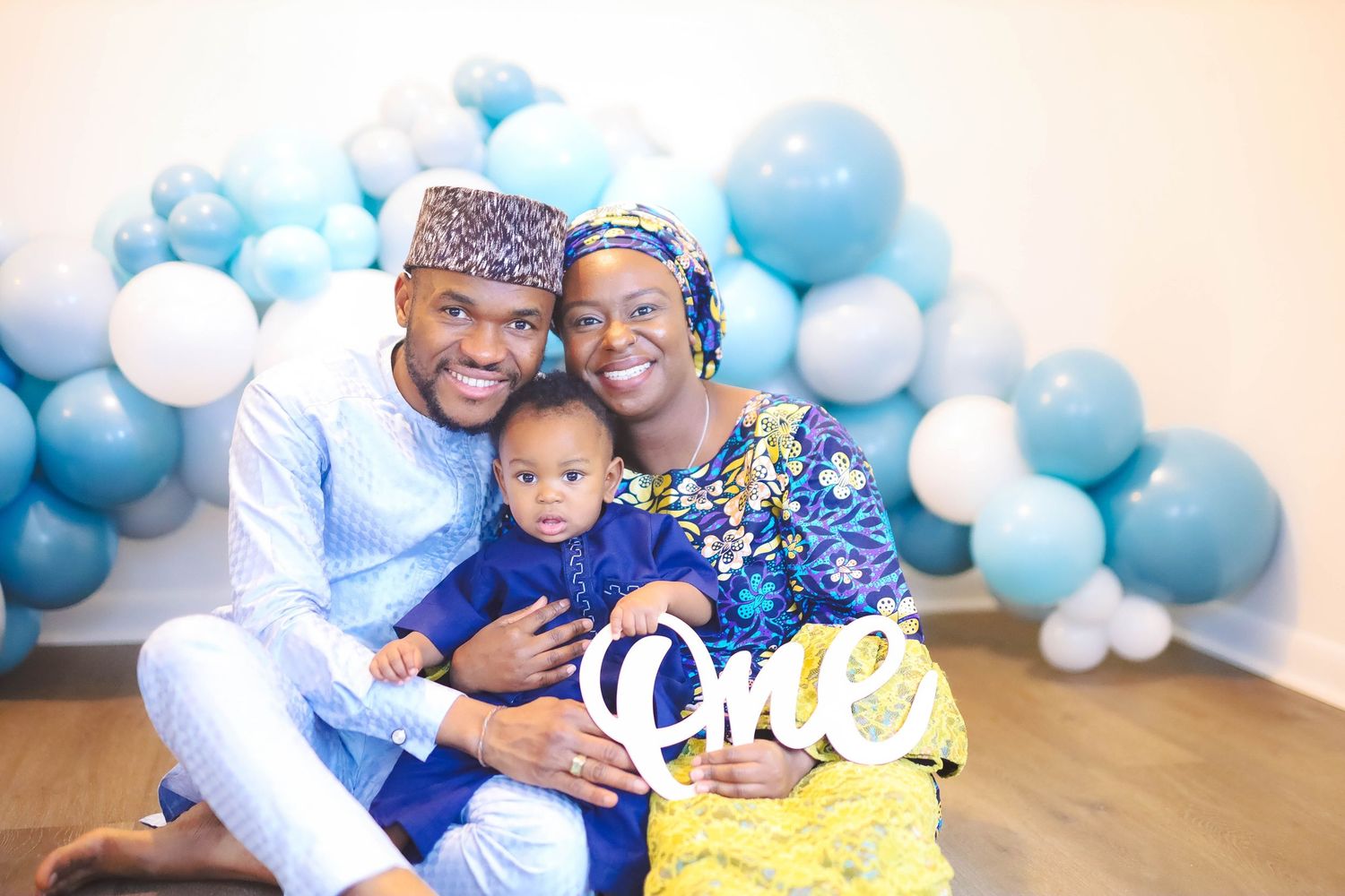 Family portrait with parents and baby boy celebrating first birthday with blue balloon decor.