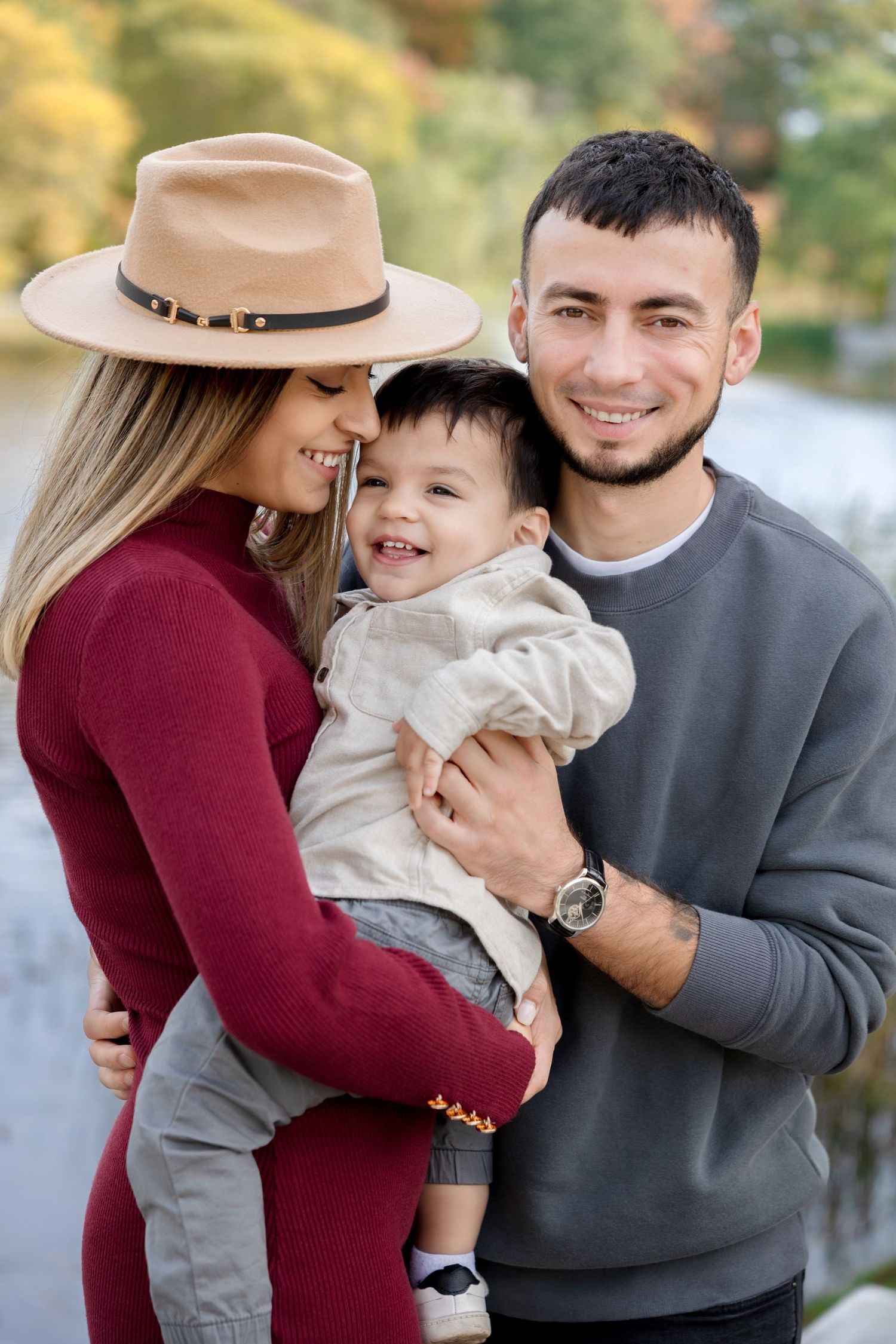 Smiling couple holding laughing toddler outdoors in fall park.