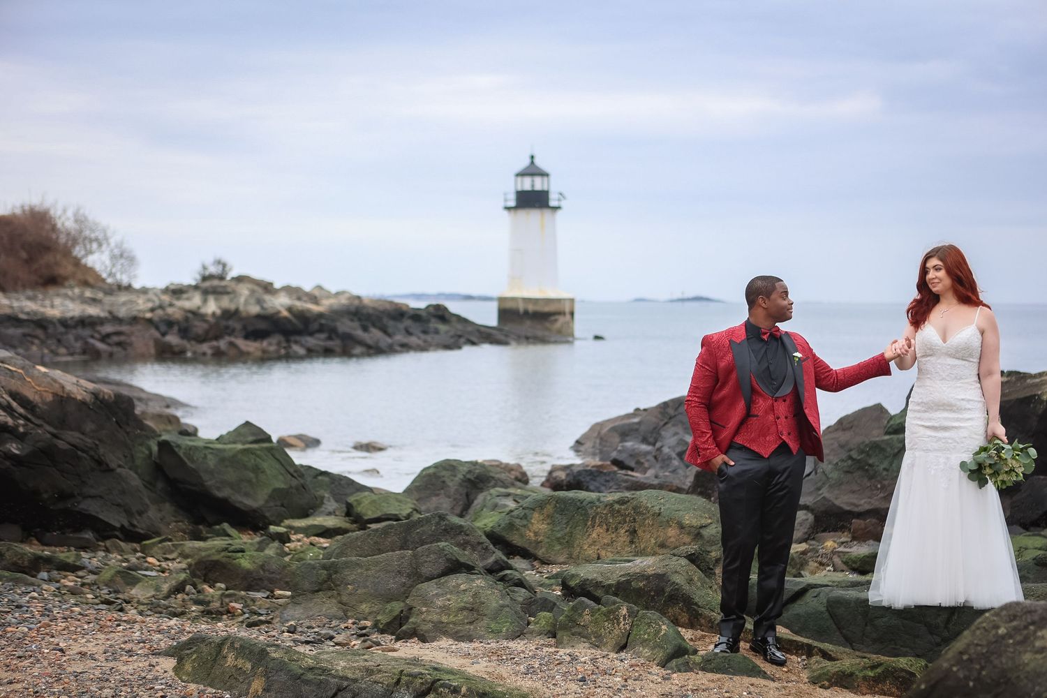 Bride and groom walking on rocky shore near Scituate Lighthouse in Scituate, Massachusetts, captured by Grand Photo by Karyna Oliinyk