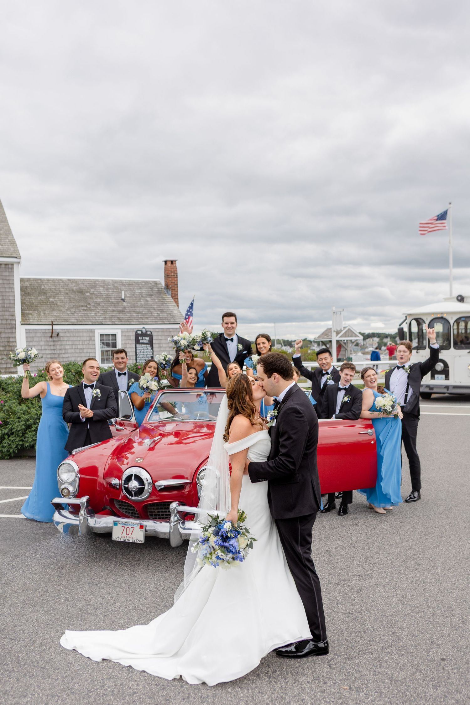 Bride and groom kiss in front of red vintage convertible at Danversport in Danvers, Massachusetts, captured by Grand Photo by Karyna Oliinyk