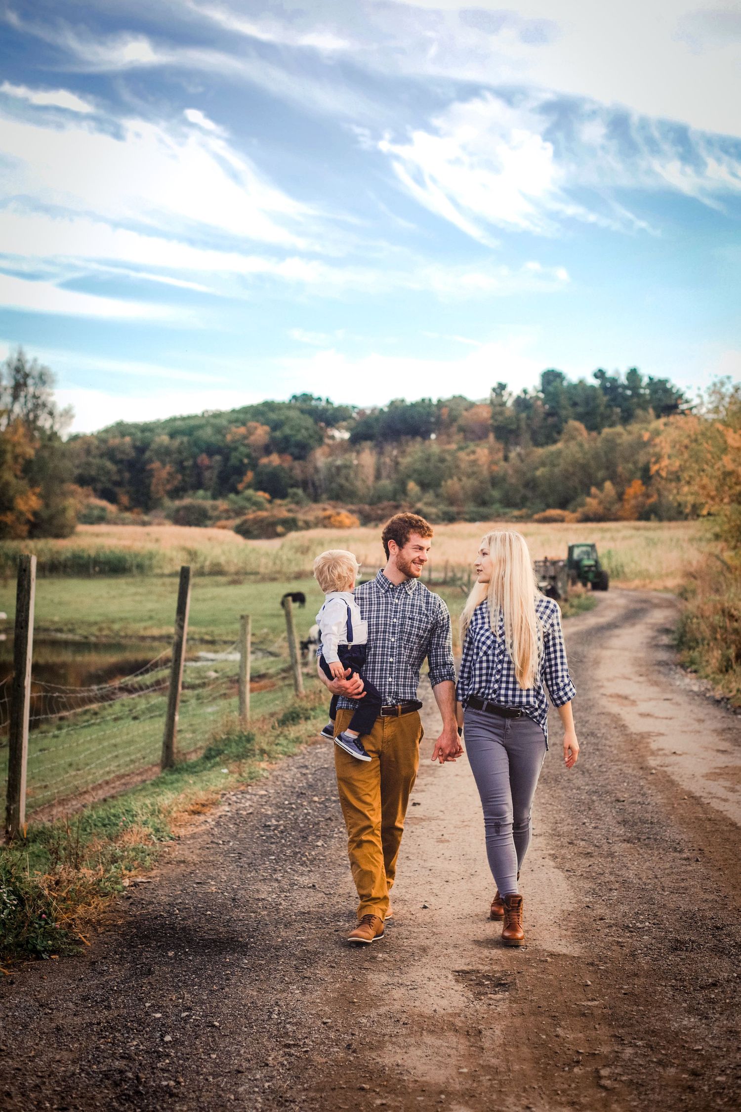 Young family walking hand-in-hand on a rural dirt road in autumn, father carrying toddler.