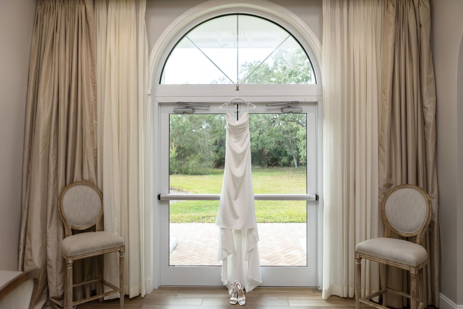Elegant wedding dress hanging with garden view at Harborside Chapel in Safety Harbor, FL - wedding photographer Grand Photo, Karyna Oliinyk
