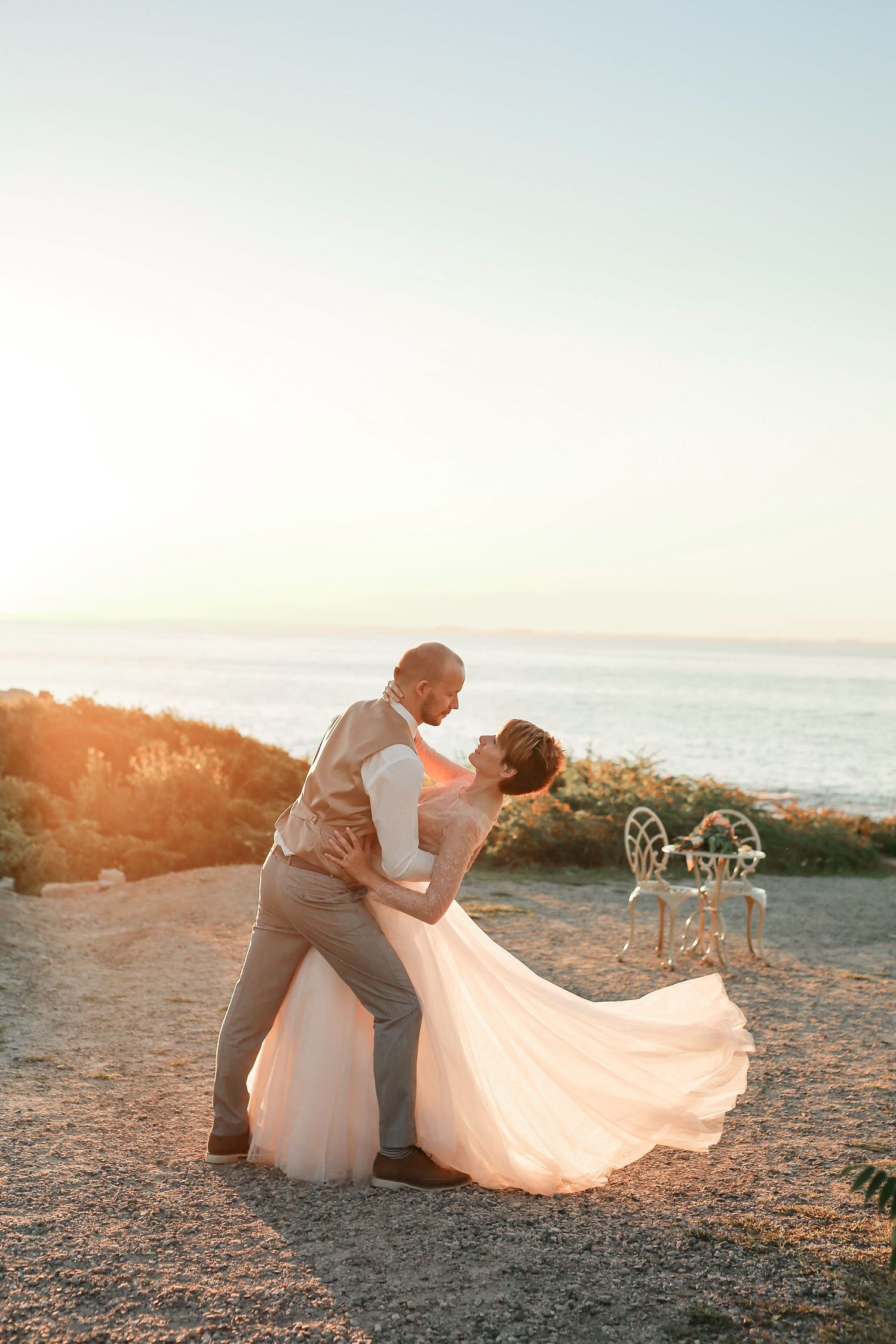 Groom dips bride in flowing dress during golden sunset at Halibut Point State Park in Rockport, Massachusetts, captured by Grand Photo