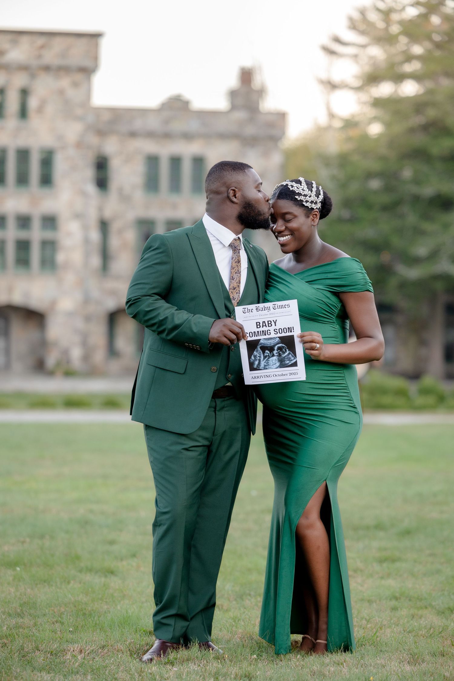 Couple in matching green outfits holding a baby announcement newspaper during an outdoor maternity photoshoot.