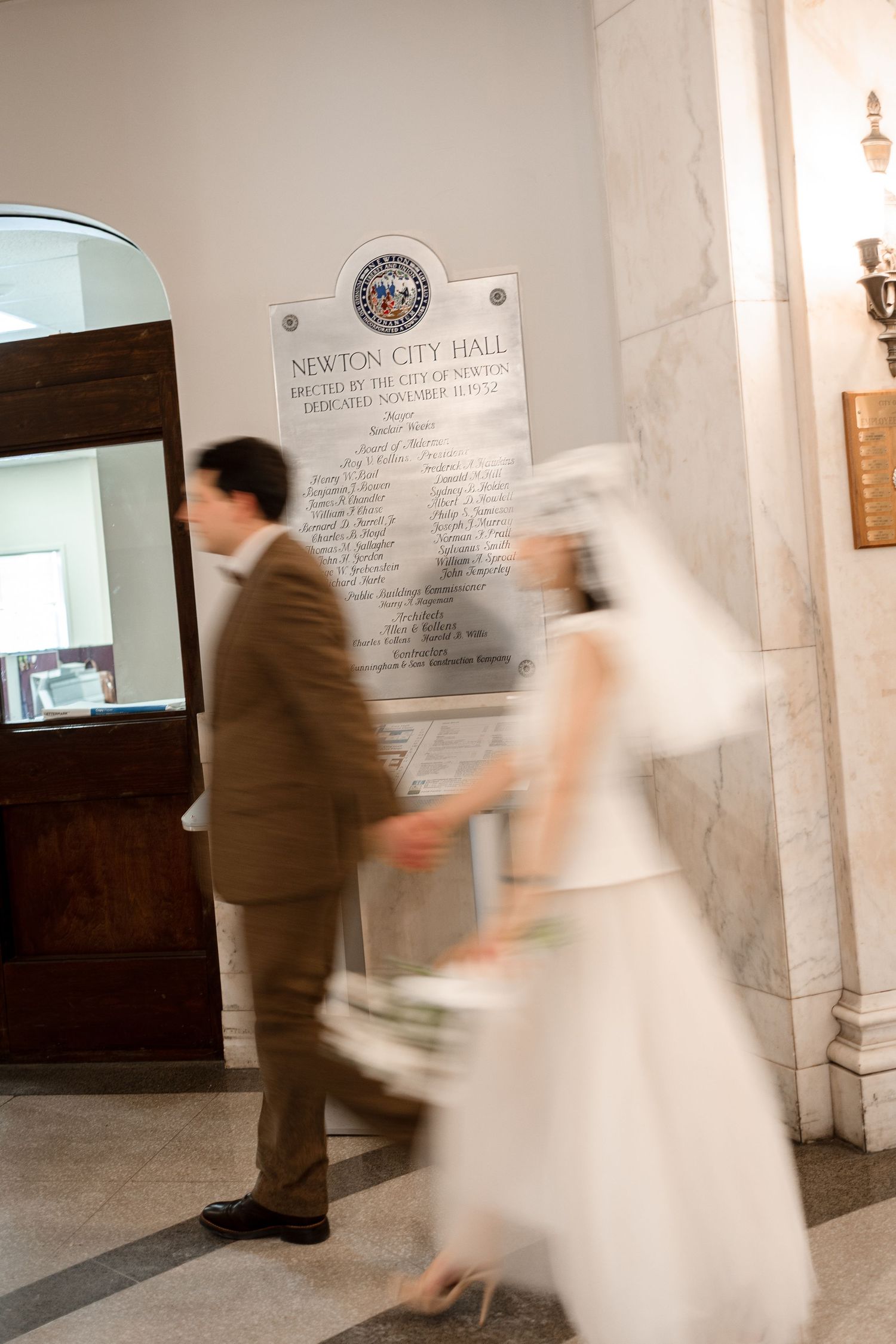 Blurred motion shot of bride and groom walking through Newton City Hall corridor captured by Grand Photo by Karyna Oliinyk