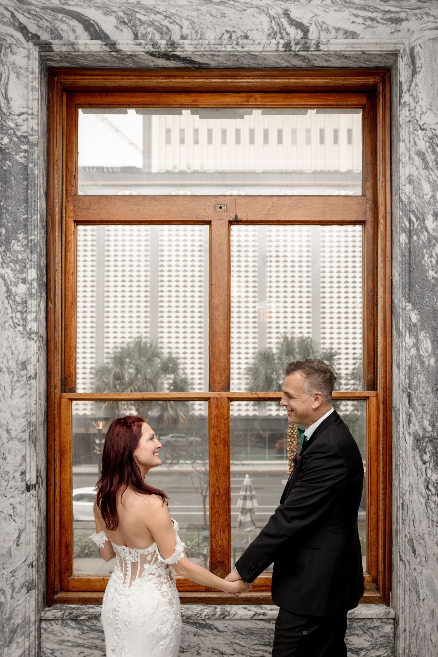 Bride and groom hold hands smiling by ornate marble window at Le Méridien Tampa, Florida, captured by Grand Photo by Karyna Oliinyk