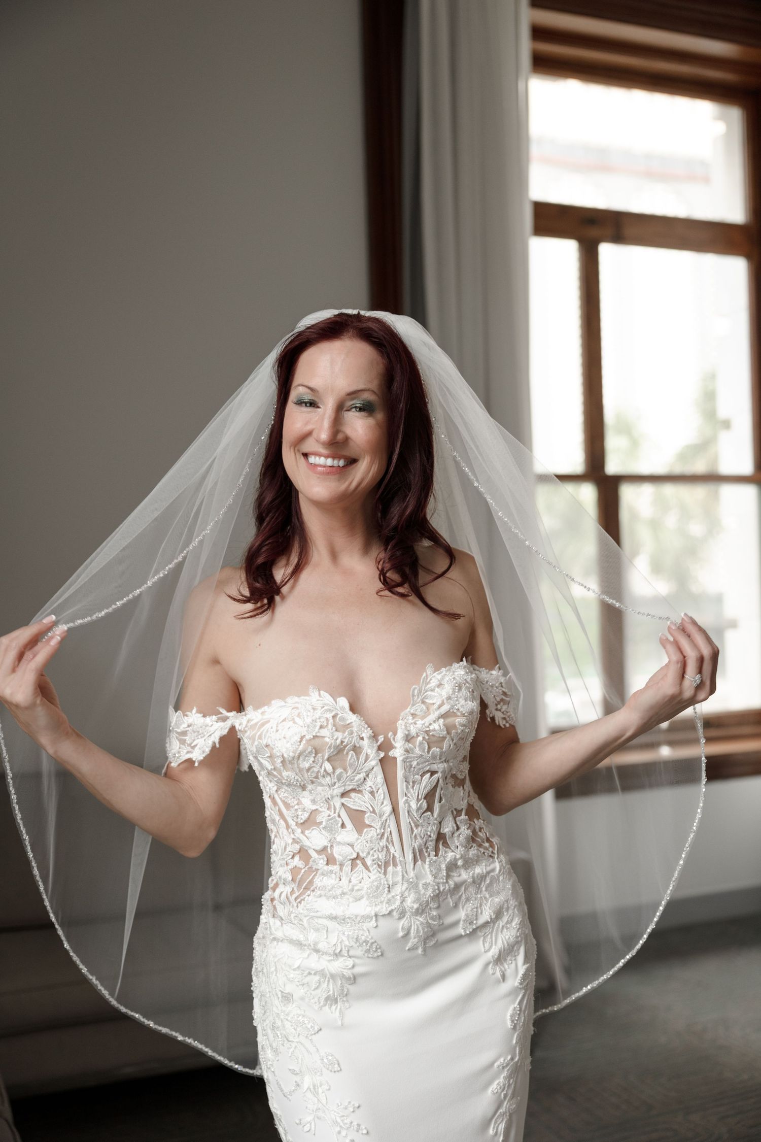 Smiling bride in off-shoulder lace wedding gown holding her veil at Le Méridien Tampa, Florida, captured by Grand Photo by Karyna Oliinyk