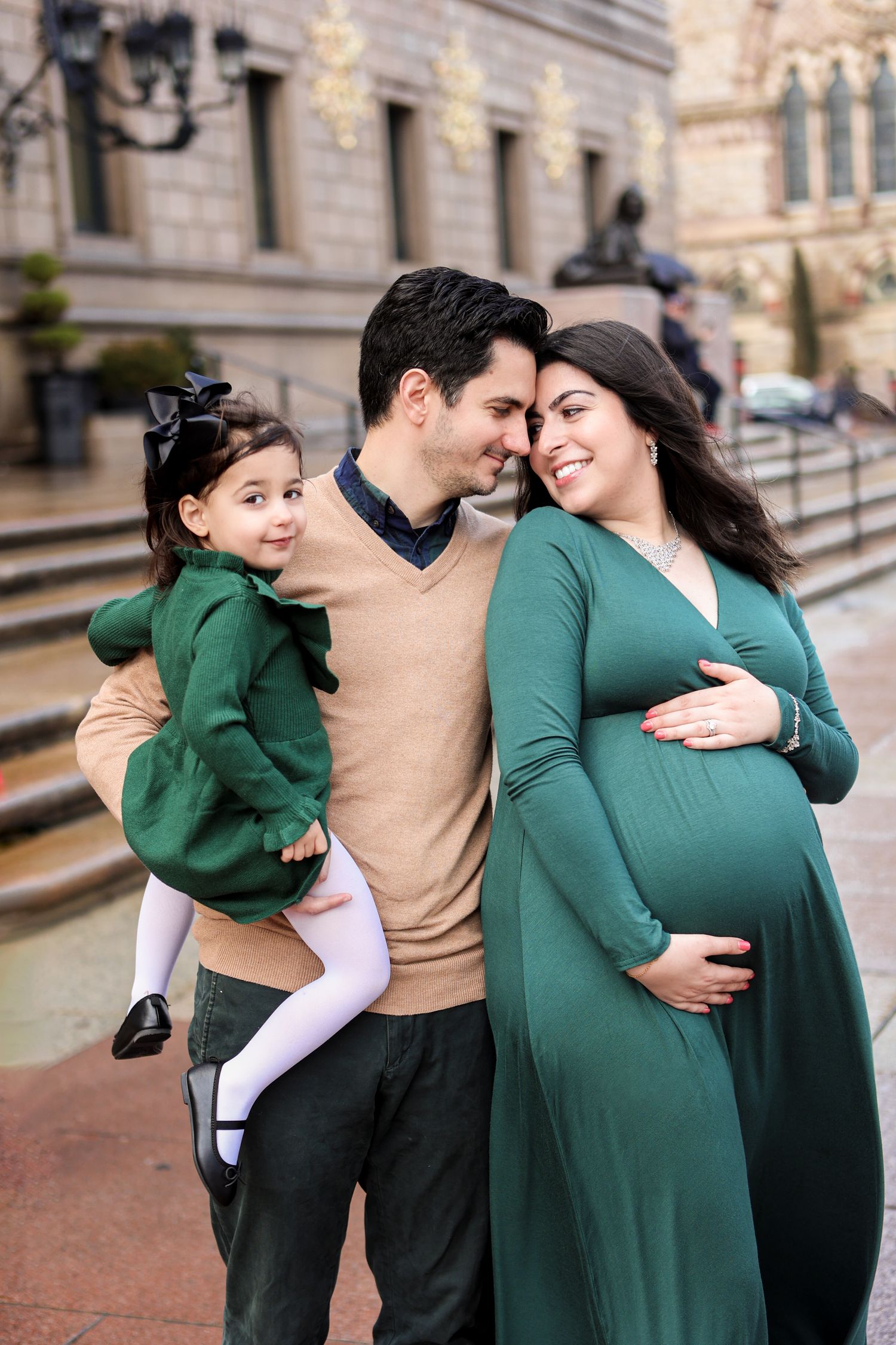 Pregnant woman in green dress with husband and daughter at outdoor maternity photo session.