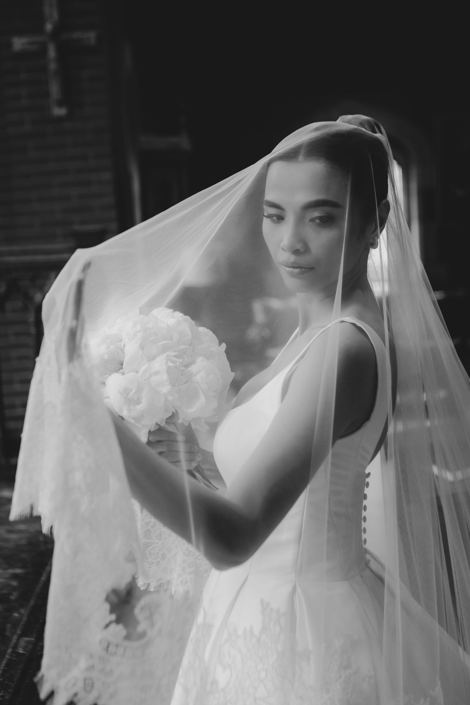Black and white portrait of a bride in a white gown and veil holding a bouquet of white flowers.