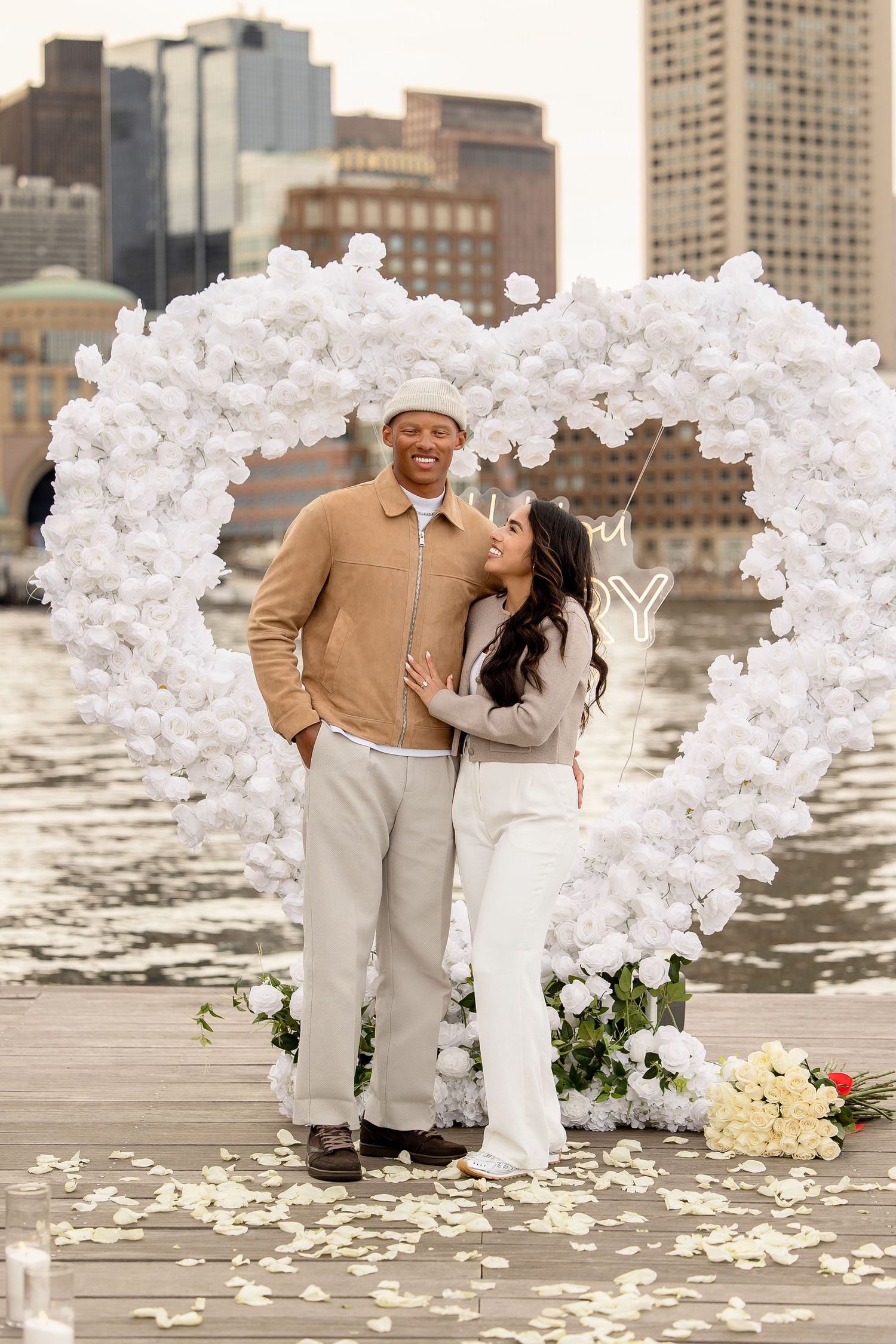 Sunset surprise proposal session with a white heart arch in Seaport Boston Massachusetts, captured by Grand Photo Karyna Oliinyk
