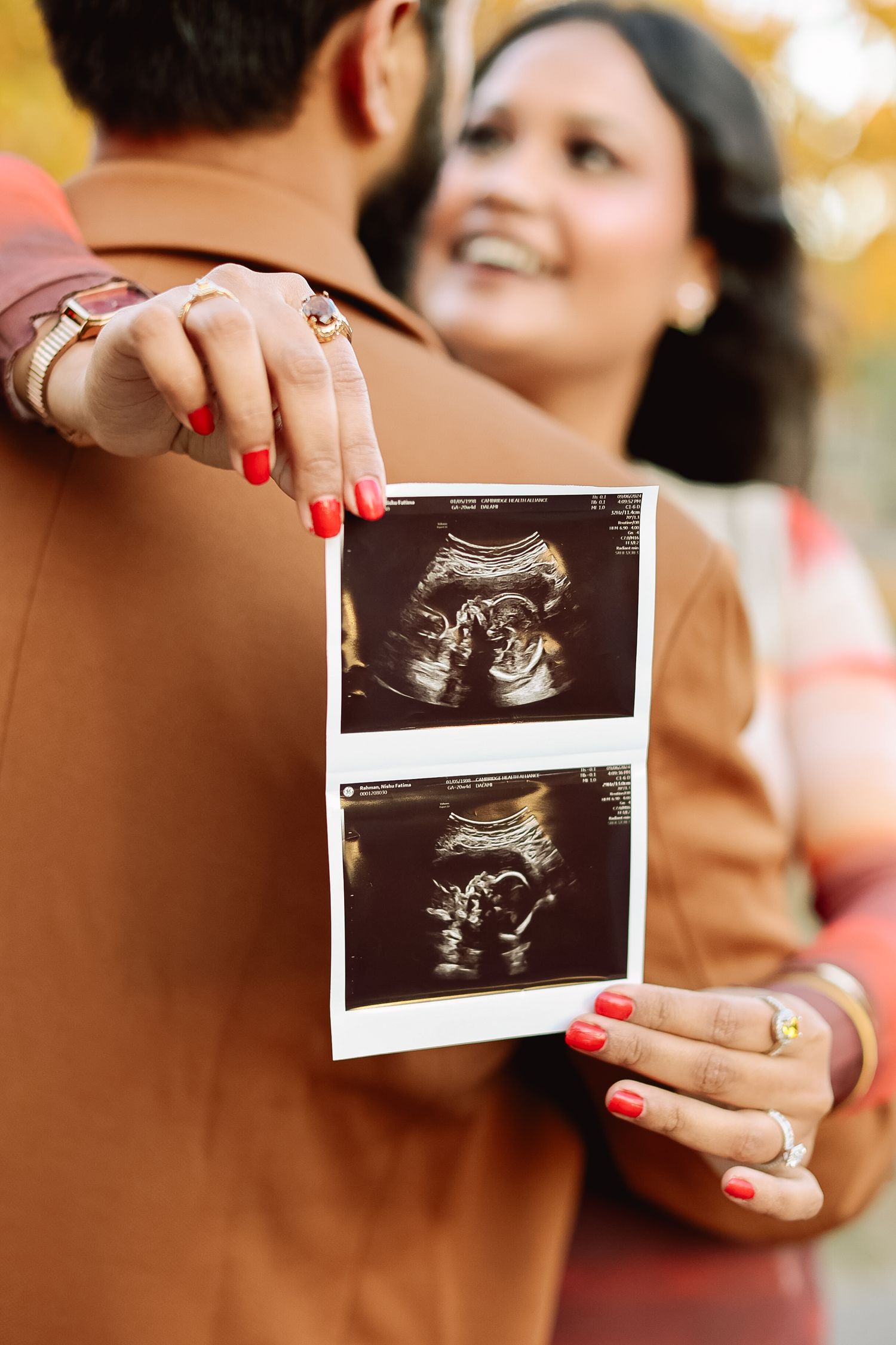 Happy couple holding ultrasound photos during fall pregnancy announcement photoshoot outdoors.