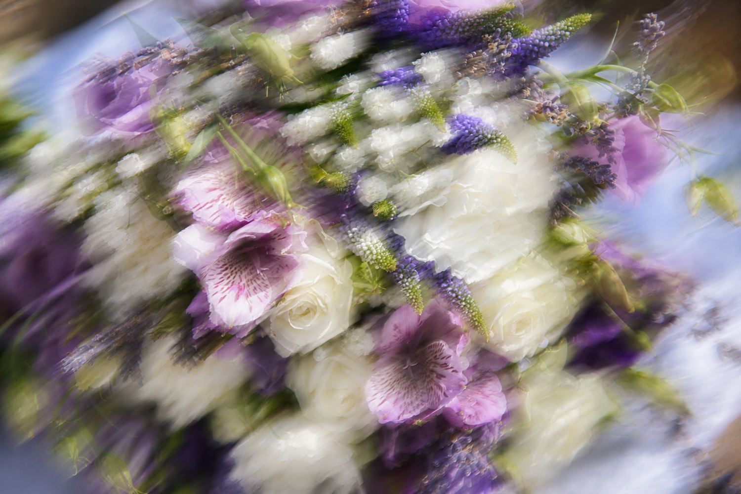 Artistic motion-blurred close-up of a purple and white wedding bouquet with roses and wildflowers.