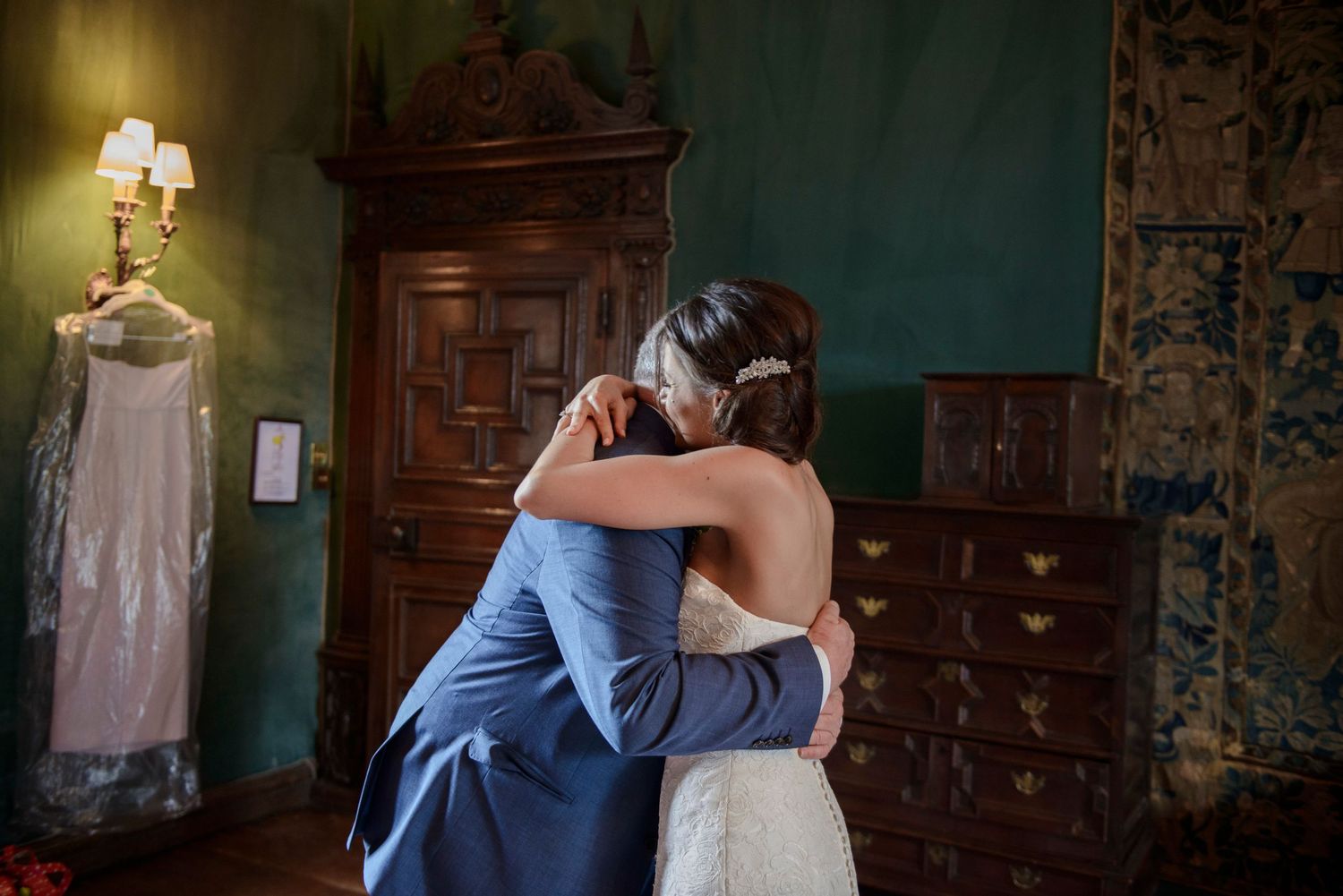 Bride and groom share an emotional embrace in an elegant room with antique wooden furniture.