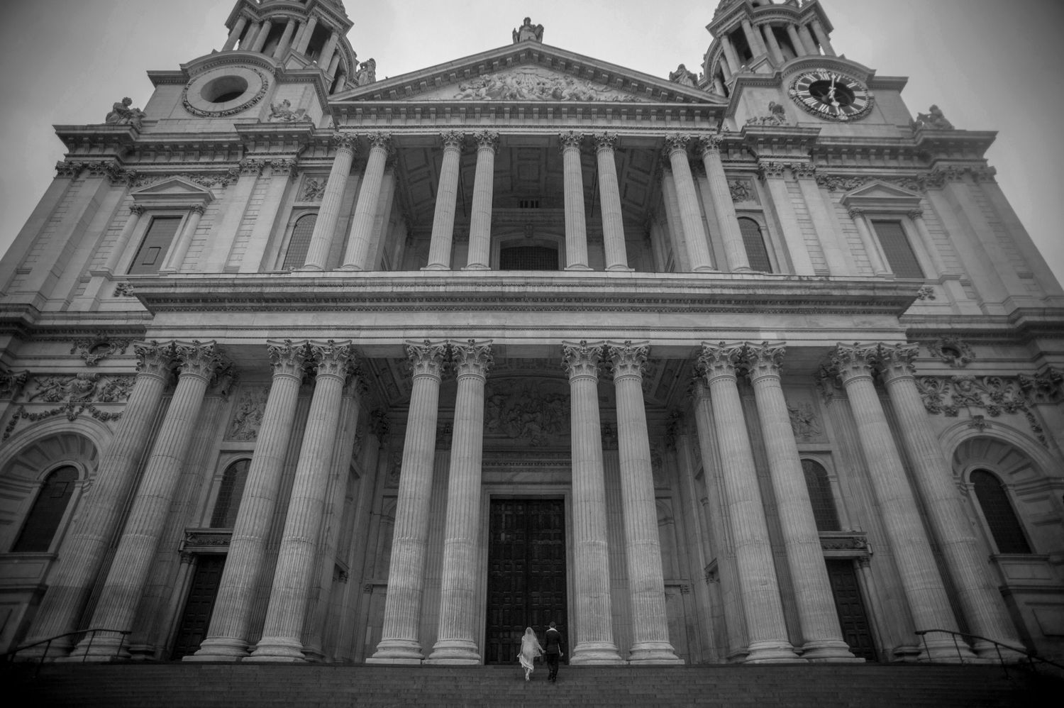 Black and white exterior view of St Pauls Cathedral London with couple on steps.