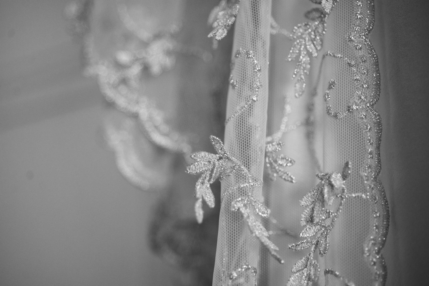 Close-up of intricate beaded lace wedding veil with delicate floral embroidery in black and white.