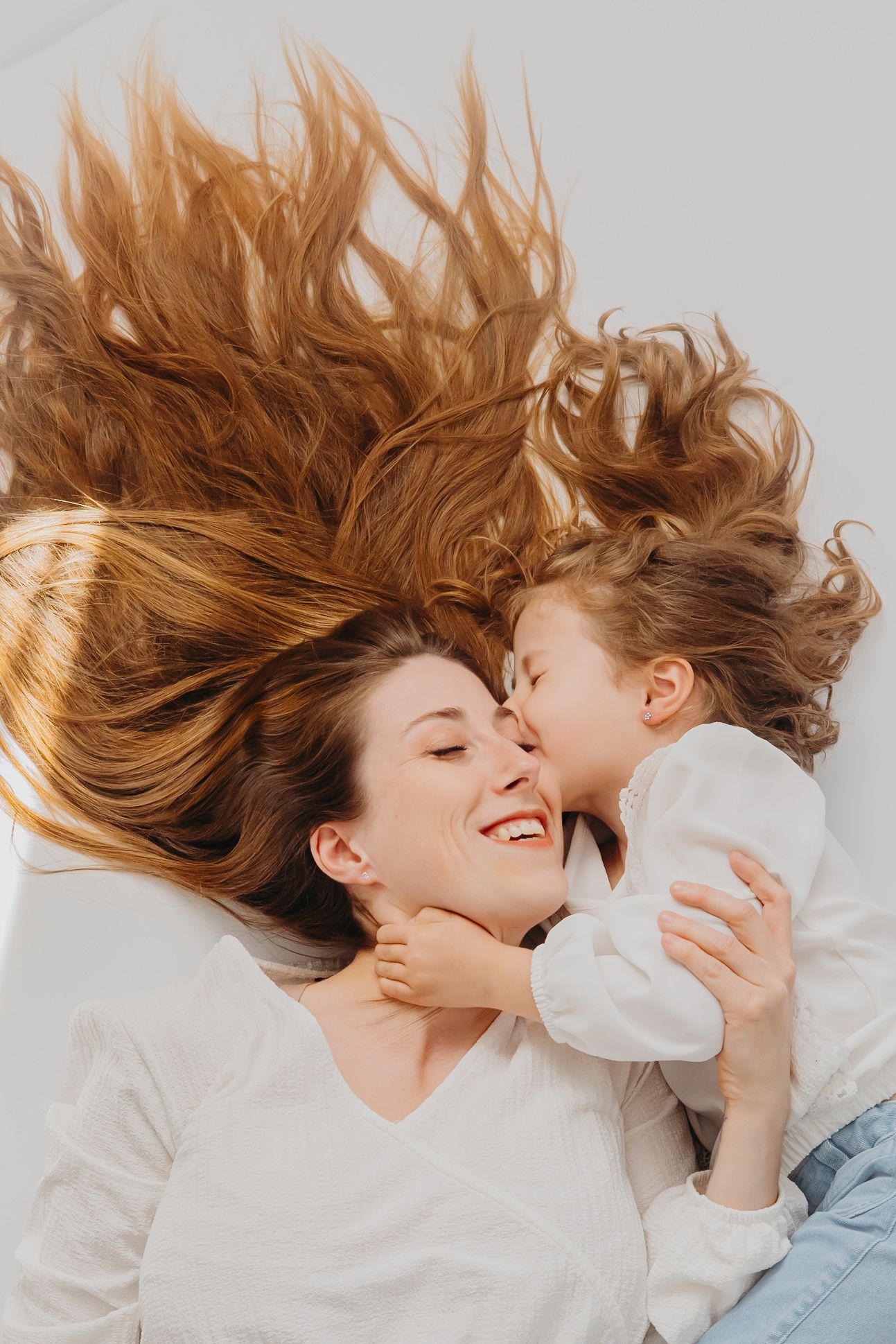 Mother and child lying down with flowing hair spread out on white background.