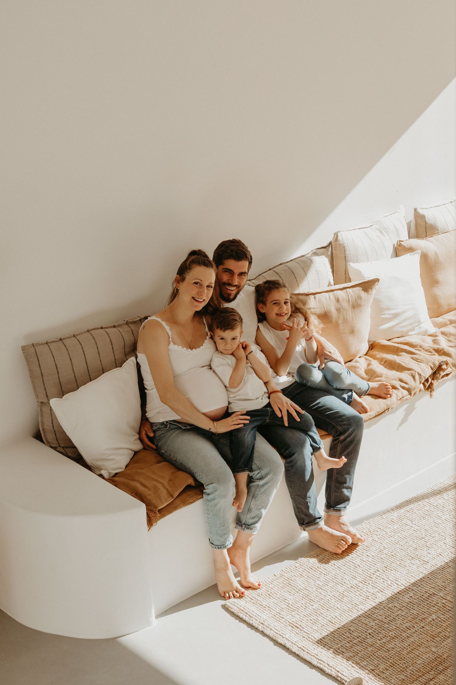 Family relaxing together on a cozy white bench with throw pillows.