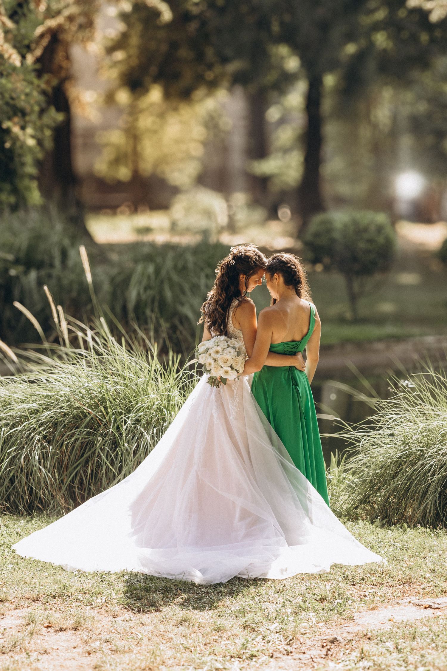 Two people in wedding attire sharing an intimate moment in a sunlit garden.