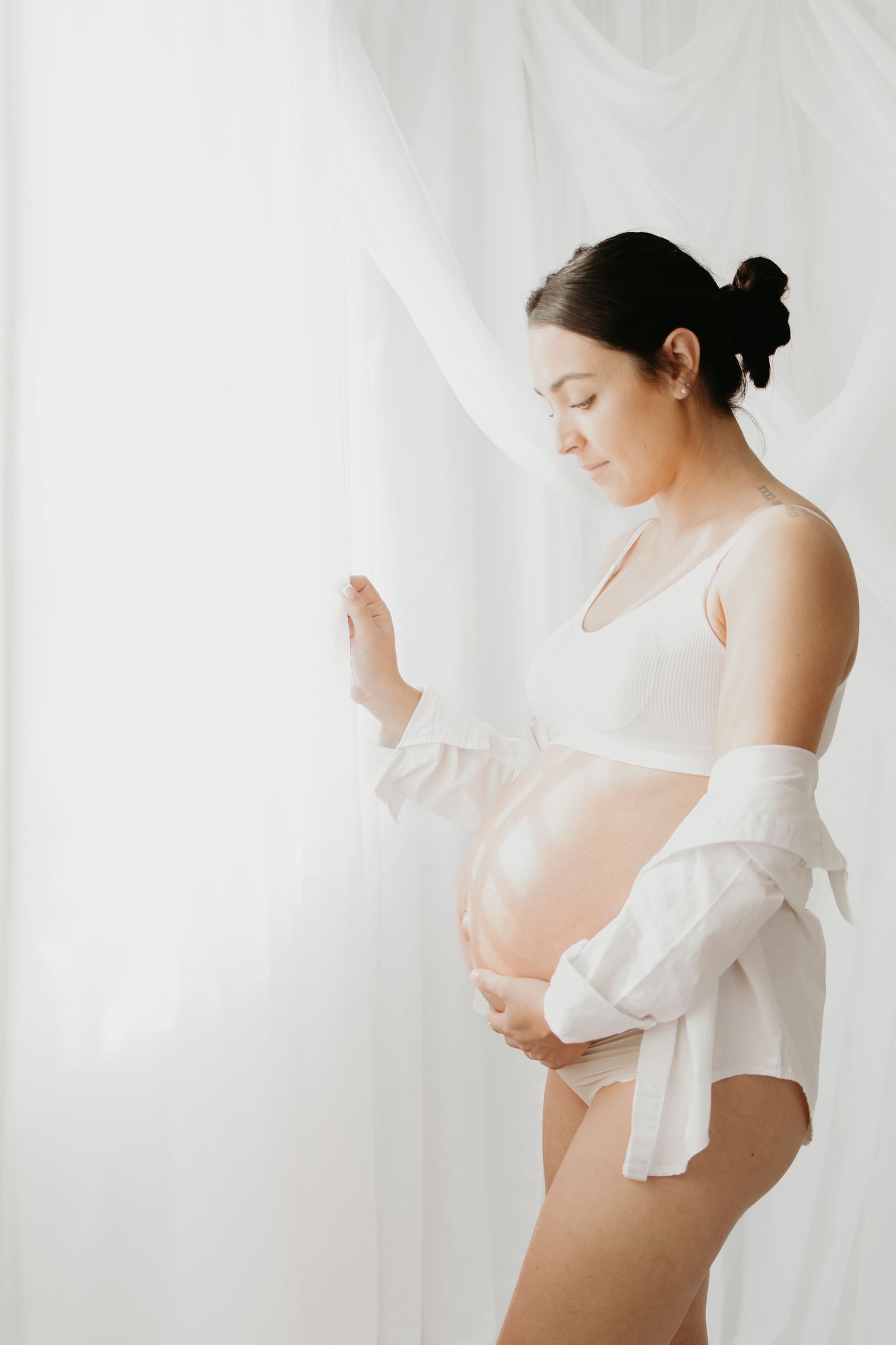A serene maternity portrait with white drapes and soft lighting.