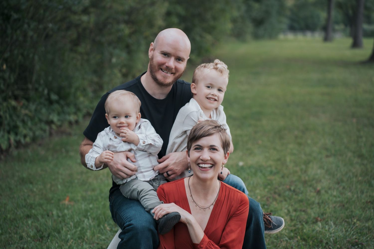 A happy family of four poses together outdoors on green grass during a casual photo session.