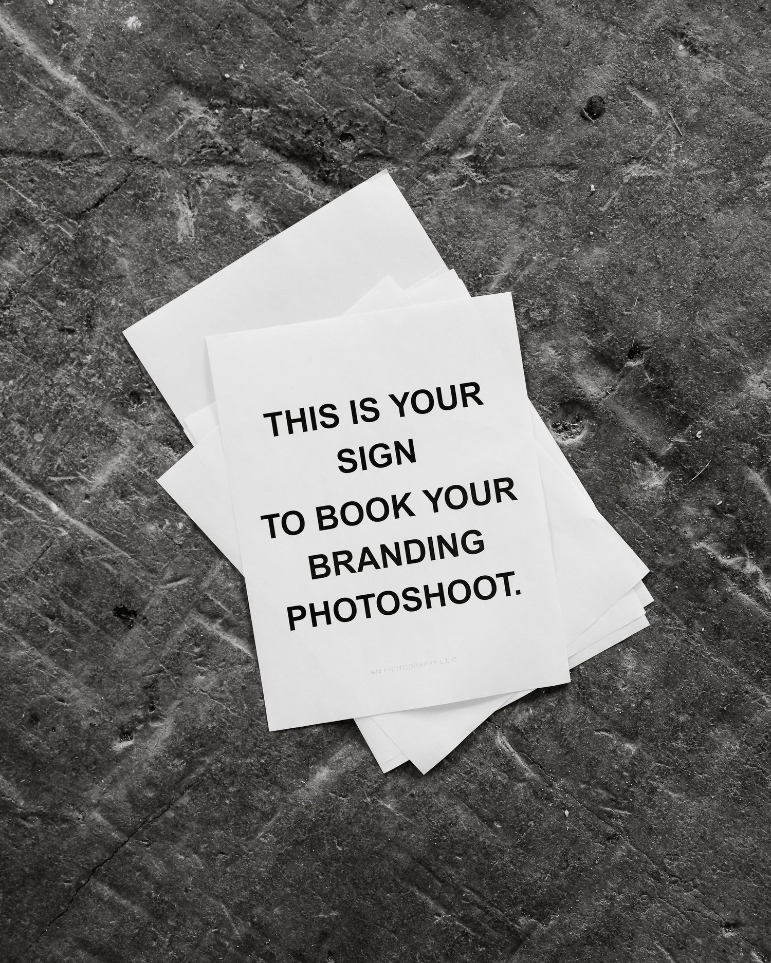 A black and white photo of a note reading 'THIS IS YOUR SIGN TO BOOK YOUR BRANDING PHOTOSHOOT' on a textured surface.