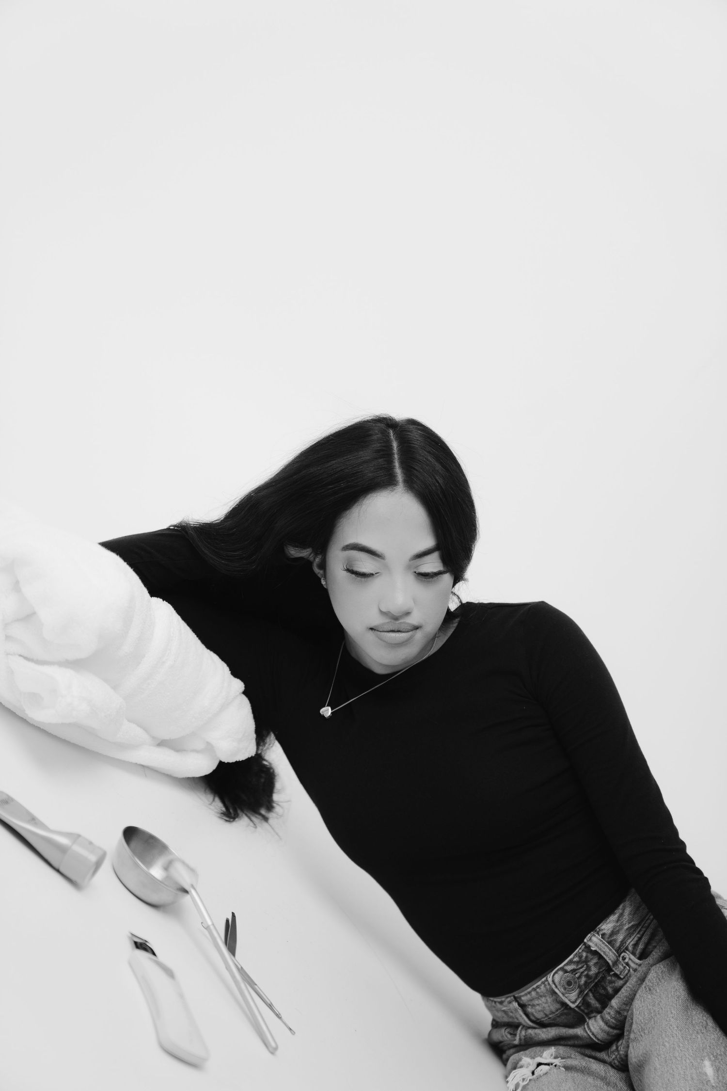 High contrast black and white portrait of person in black turtleneck and jeans laying against white background.