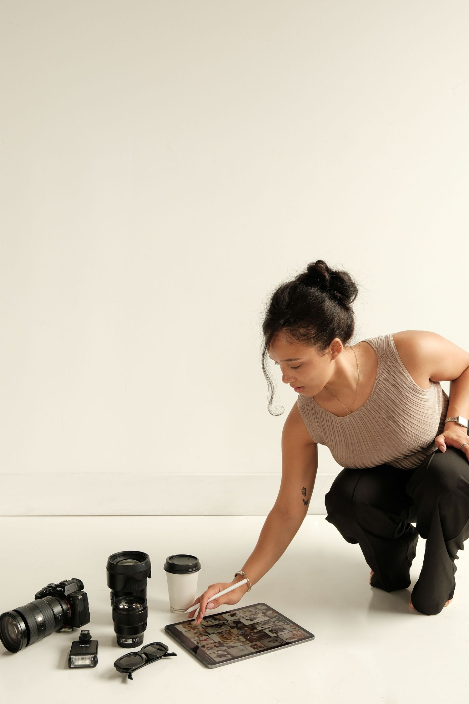 Photographer crouching next to photography equipment including camera lenses and digital tablet on white floor.