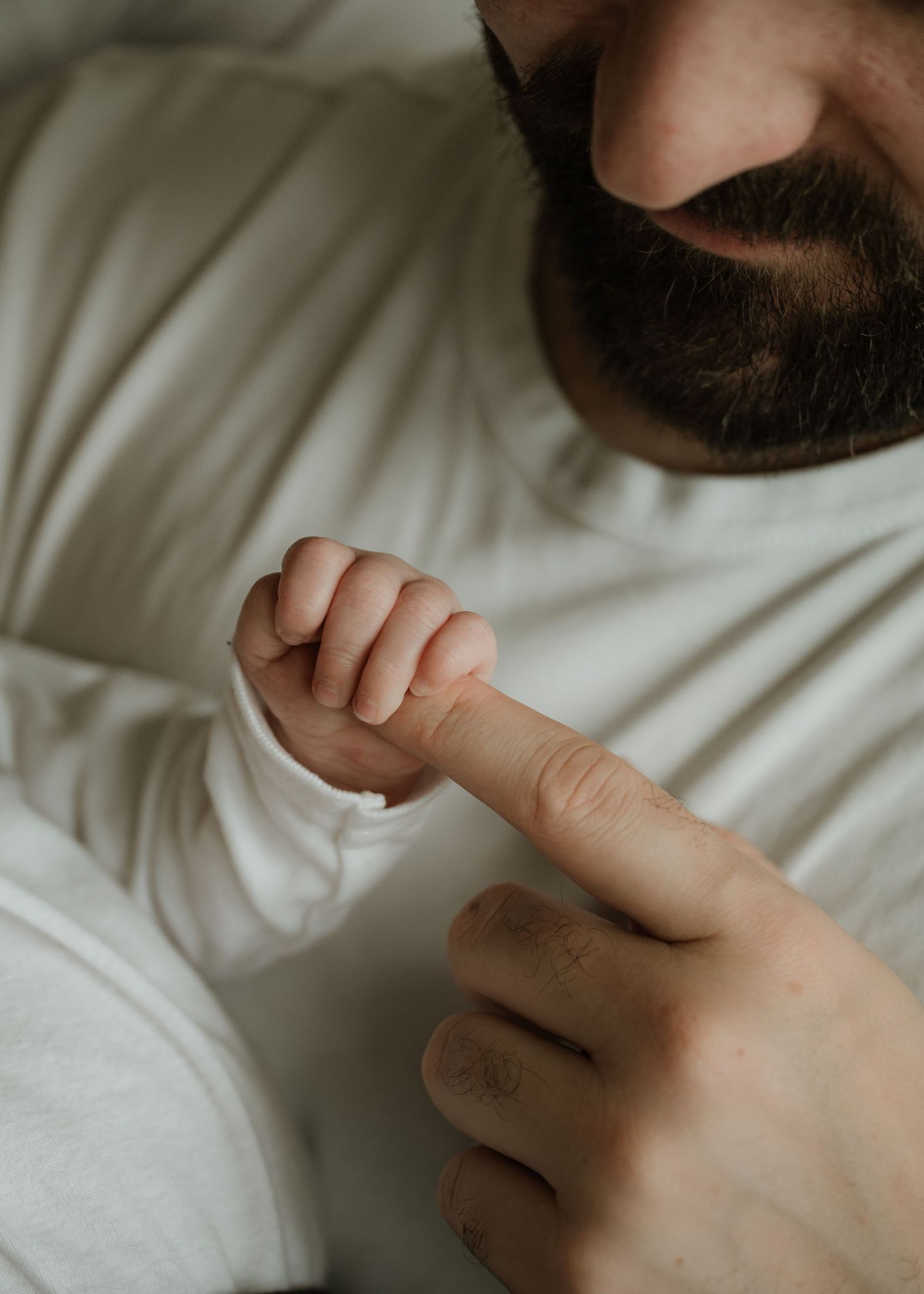 Newborn baby's tiny hand grips the finger of a bearded father in a close-up, tender bonding moment.