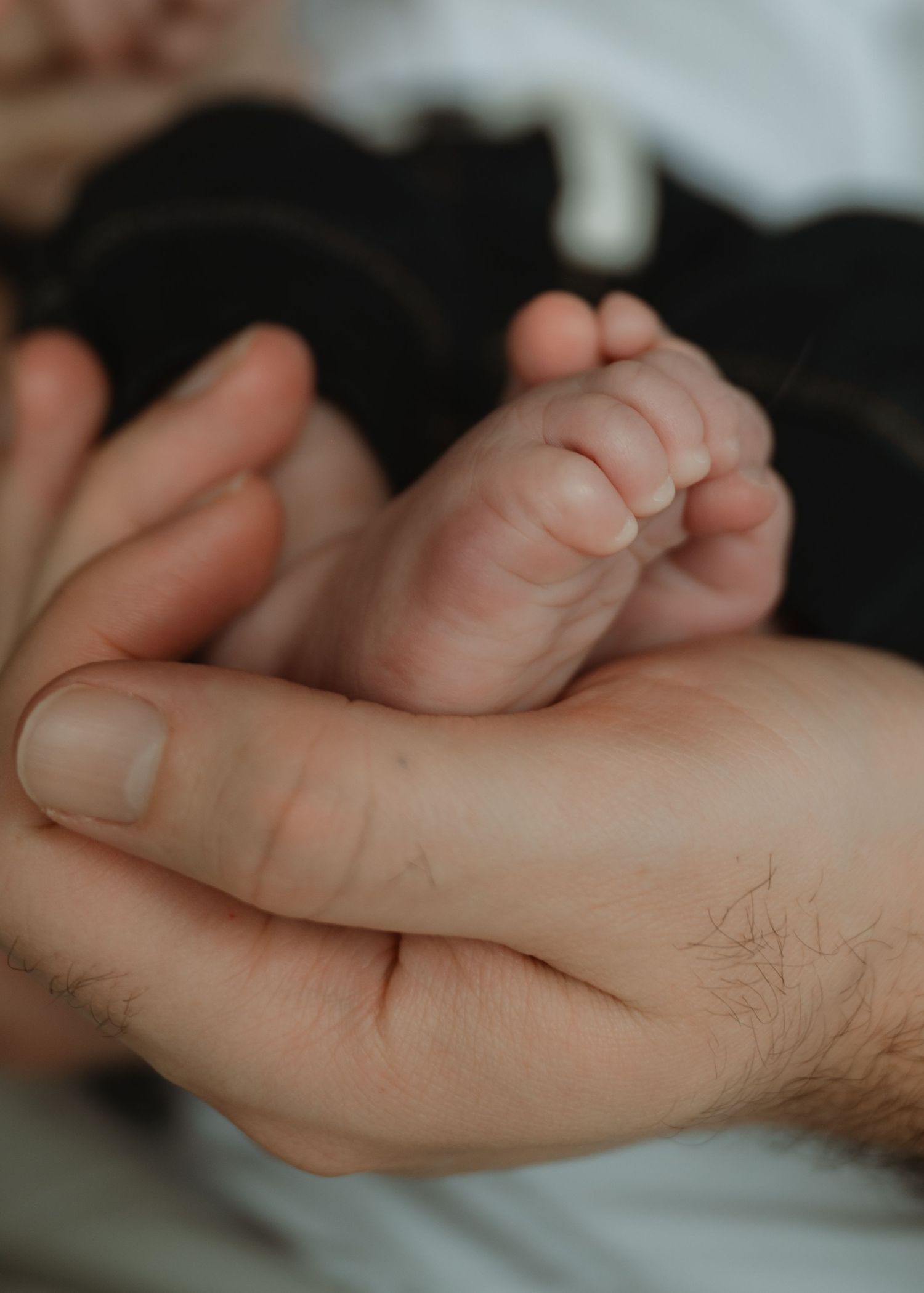 Close-up of a father's large hands gently cupping a newborn baby's tiny feet in a tender, intimate moment.