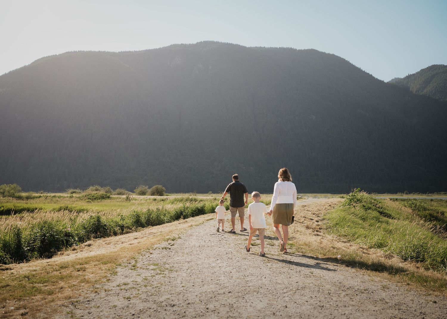 Family enjoying a leisure walk along a dirt trail with mountains in the background on a sunny afternoon.
