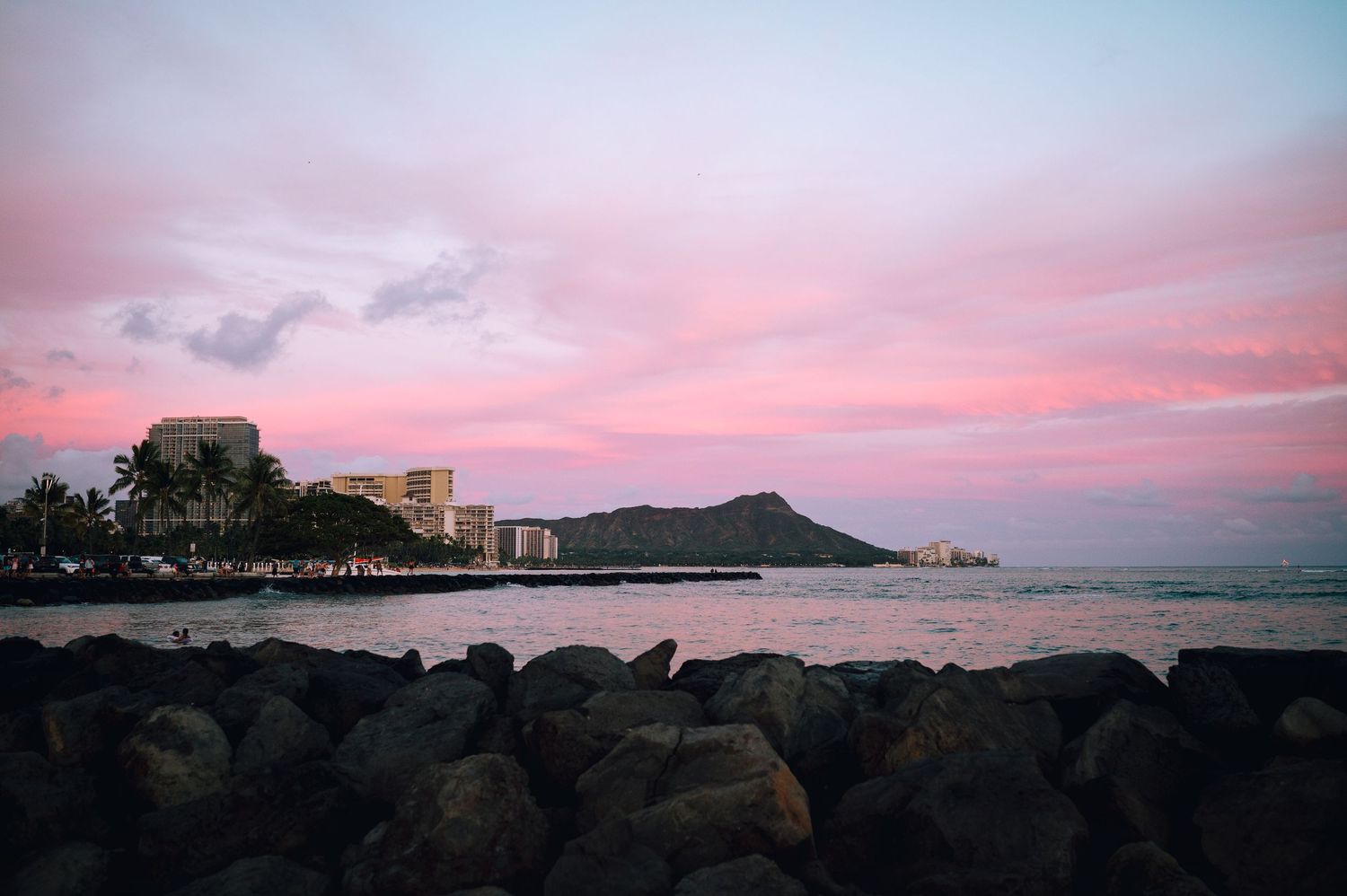 Diamond Head crater and Waikiki beach at sunset with rocky foreground in Hawaii.