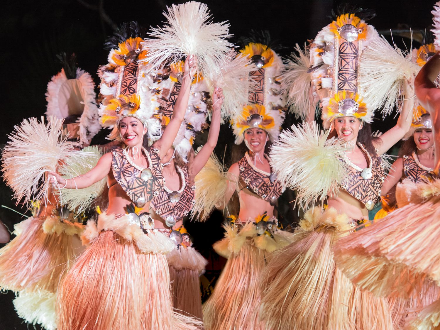 Performers in elaborate pink feathered costumes and headdresses dance in formation during a theatrical show.