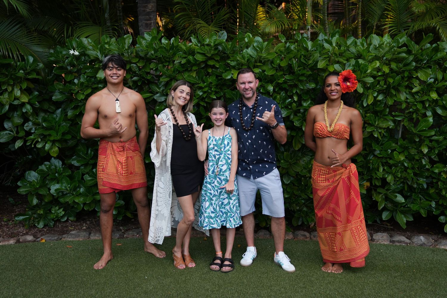 A group of people enjoying a casual outdoor gathering in a garden setting with lush green foliage in the background.