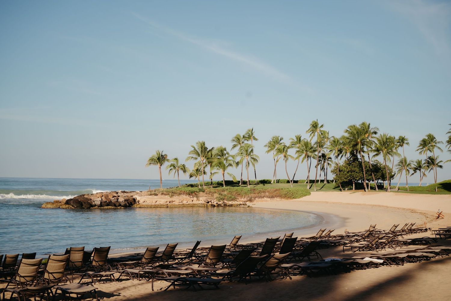 Scenic beachfront panorama with palm trees, lounge chairs, and crystal clear waters along a tropical coastline.
